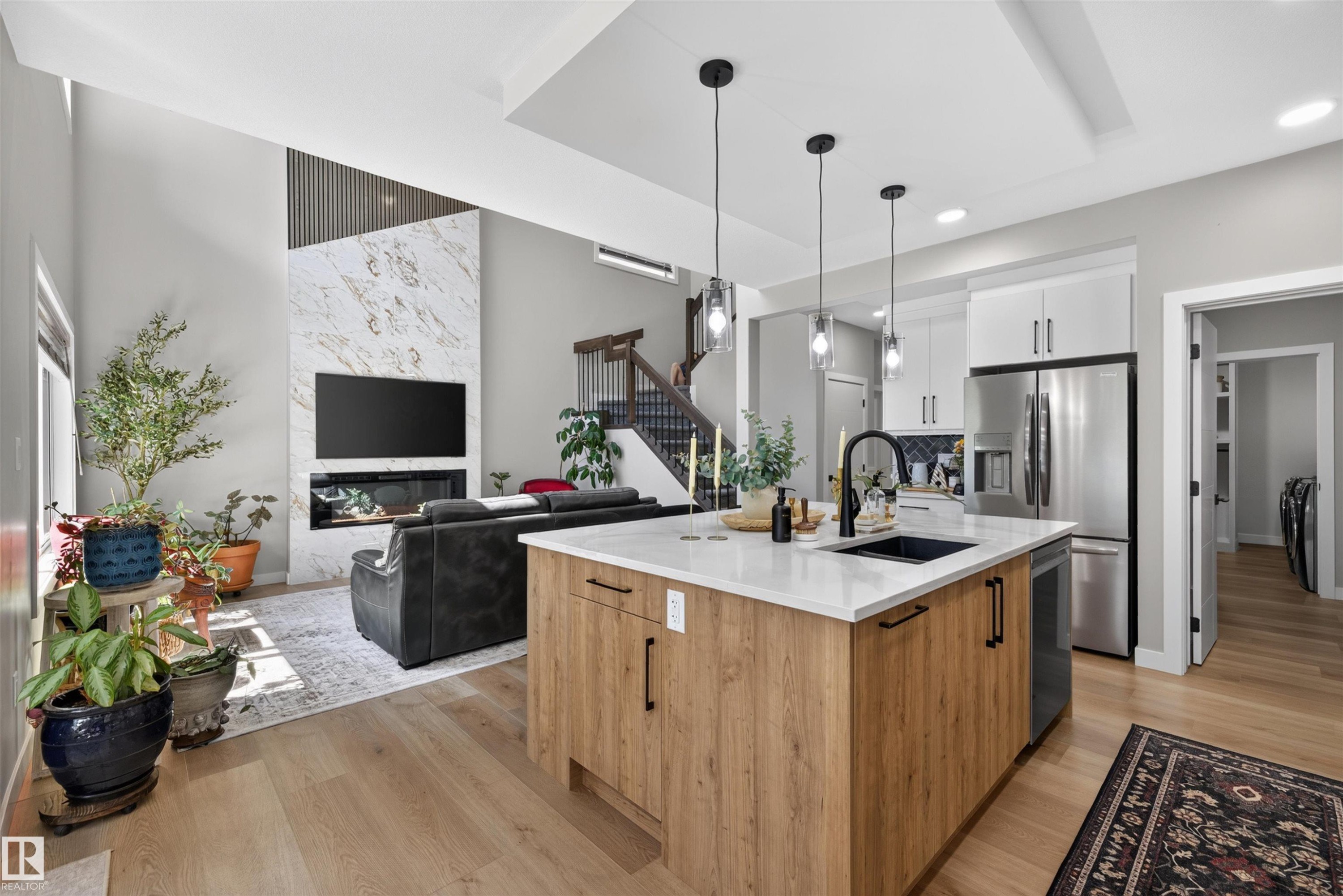 Open-concept living space featuring a central kitchen island with a dark sink, light countertops, and pendant lighting - 1573 Esaiw Place Nw, Edmonton, AB