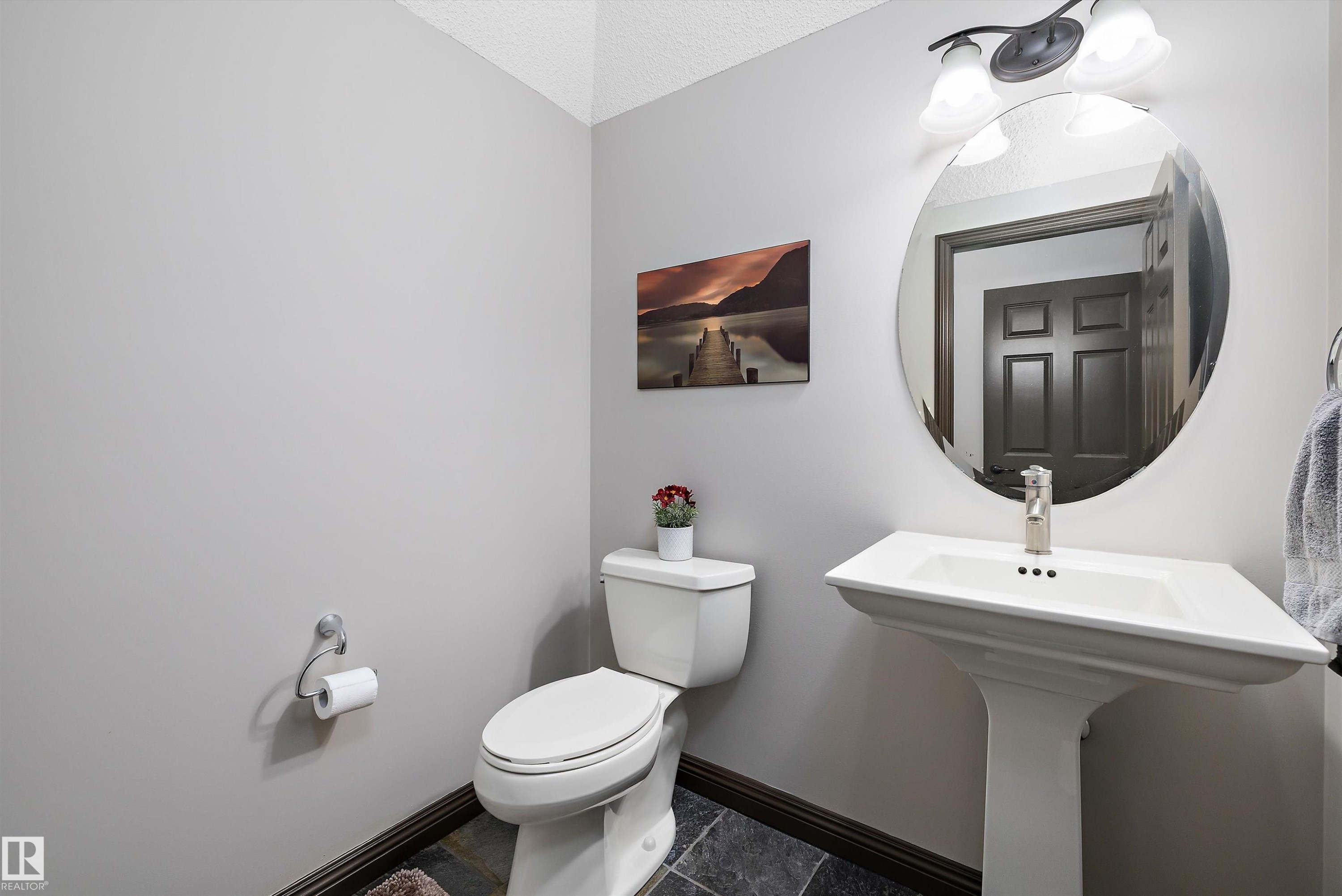 Bathroom featuring a white pedestal sink with a single-handle faucet, an oval mirror, and a two-light vanity fixture - 533 Stewart Crescent, Edmonton, AB