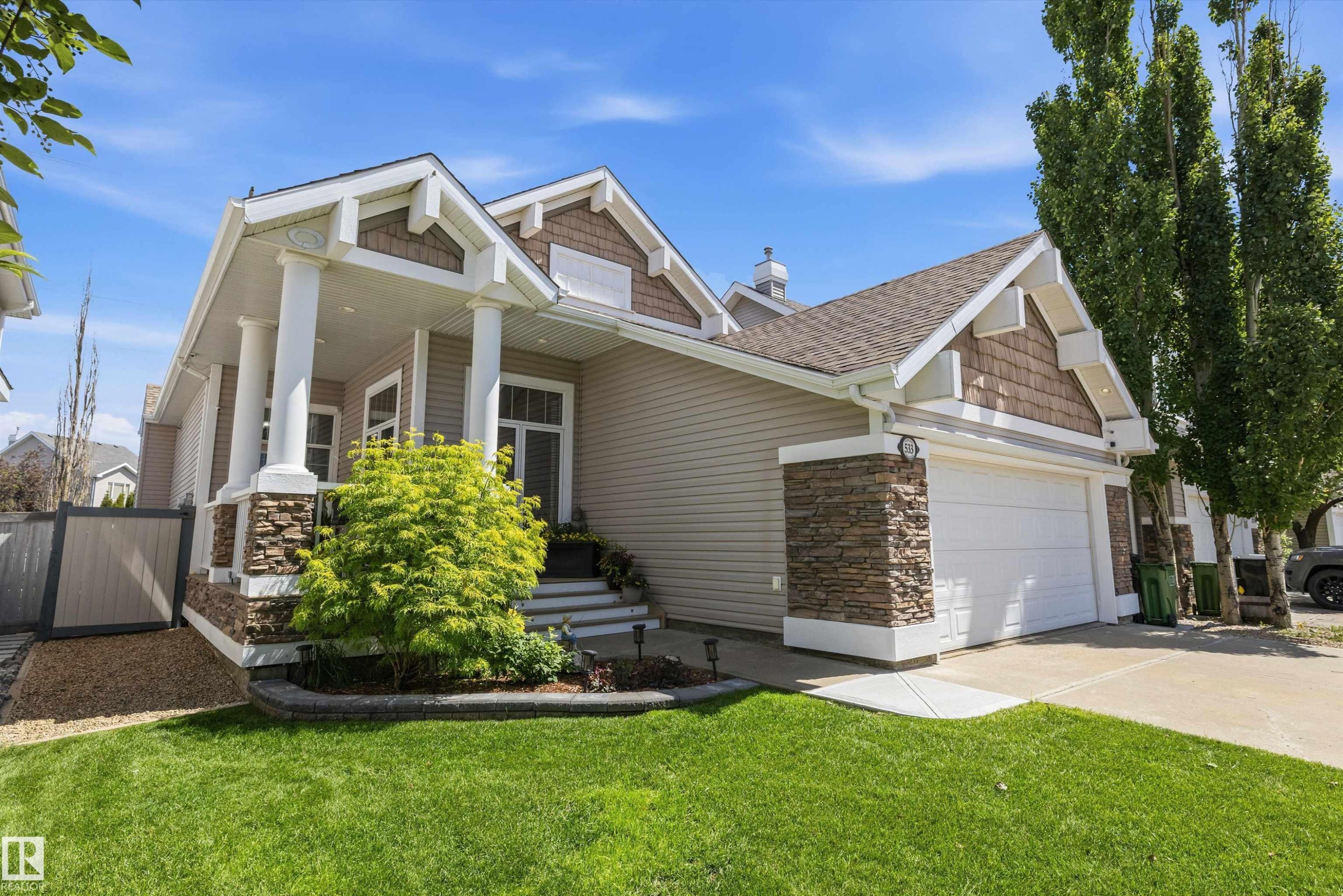 Exterior featuring a covered front porch with substantial columns, stone veneer accents, durable siding, a two-car garage with overhead door, and a manicured lawn - 533 Stewart Crescent, Edmonton, AB