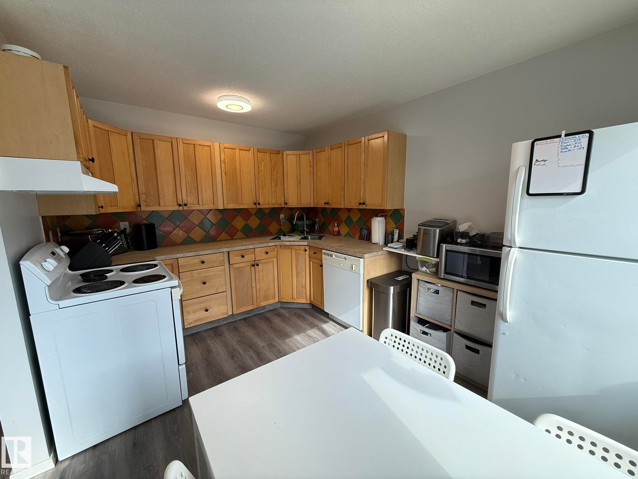 Kitchen featuring wood cabinetry, a colorful tiled backsplash, and wood-finish flooring - 166 Roseland Village, Edmonton, AB - Indoor Photo Showing Kitchen