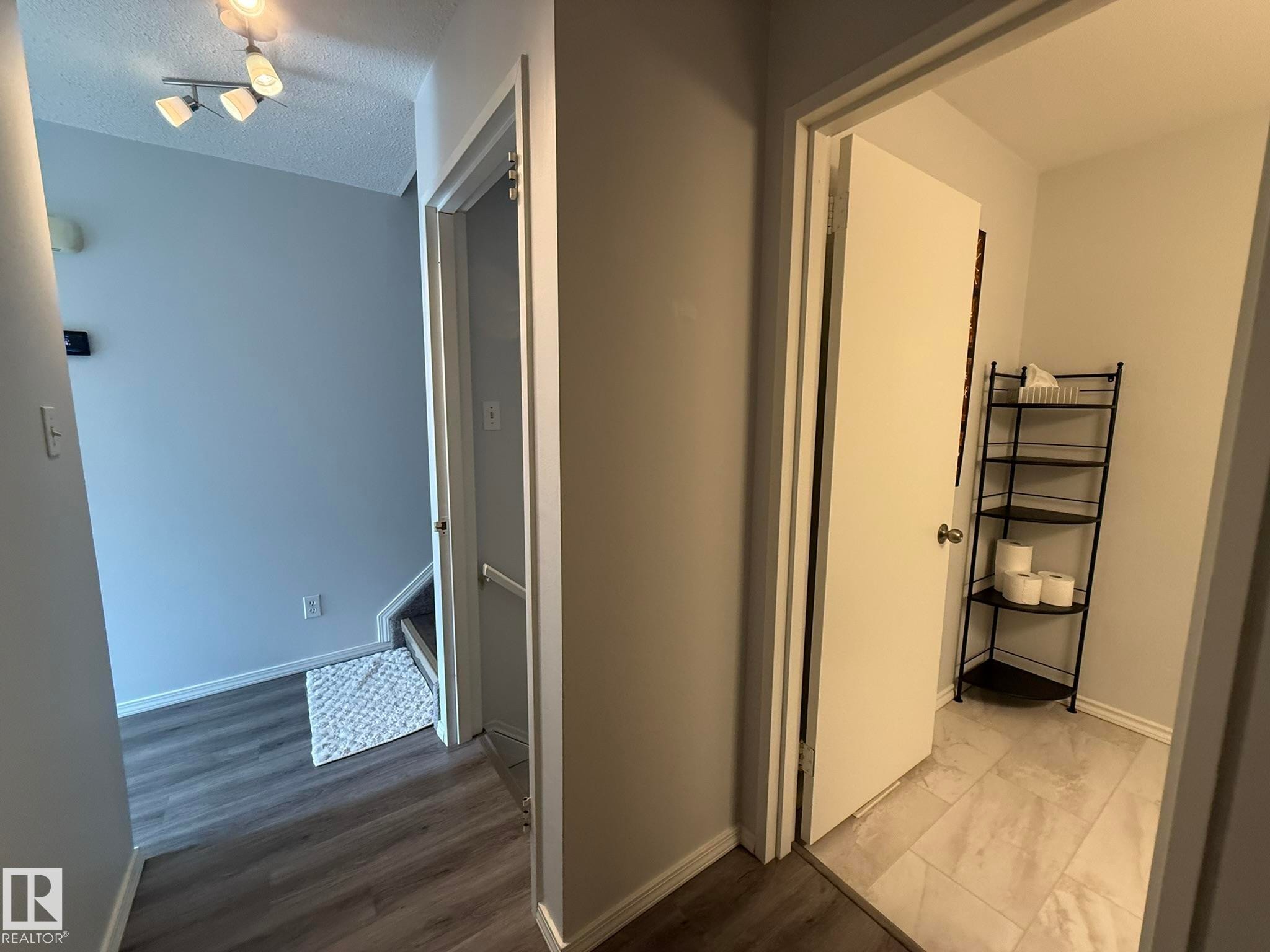 Hallway featuring wood-finish flooring, light grey wall paint, and a modern track light fixture - 166 Roseland Village, Edmonton, AB - Indoor Photo Showing Other Room