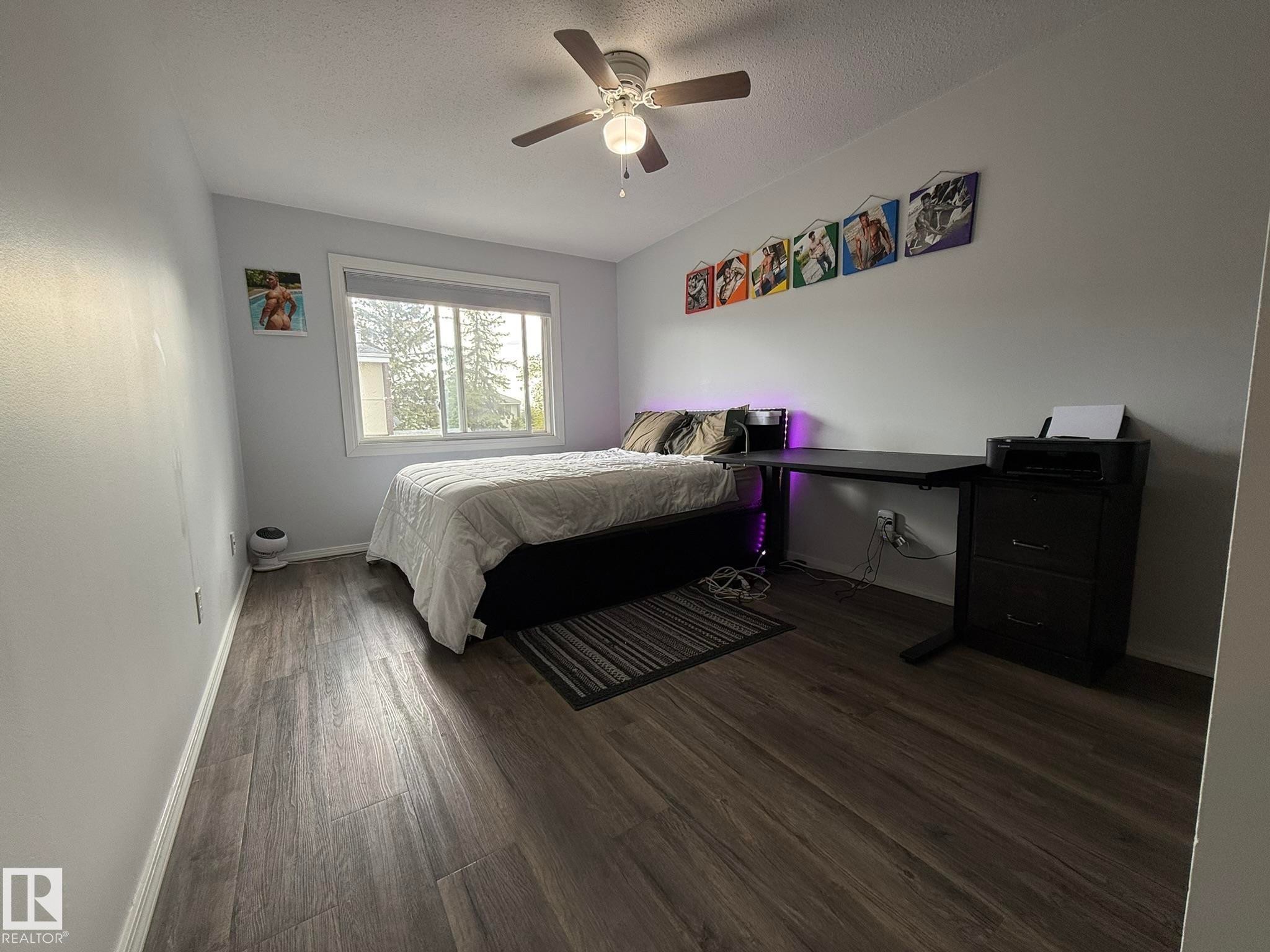 Spacious Primary Bedroomfeaturing VINYL PLANK FLOORING, a ceiling fan with integrated lighting, and a large window with white trim - 166 Roseland Village, Edmonton, AB - Indoor Photo Showing Bedroom