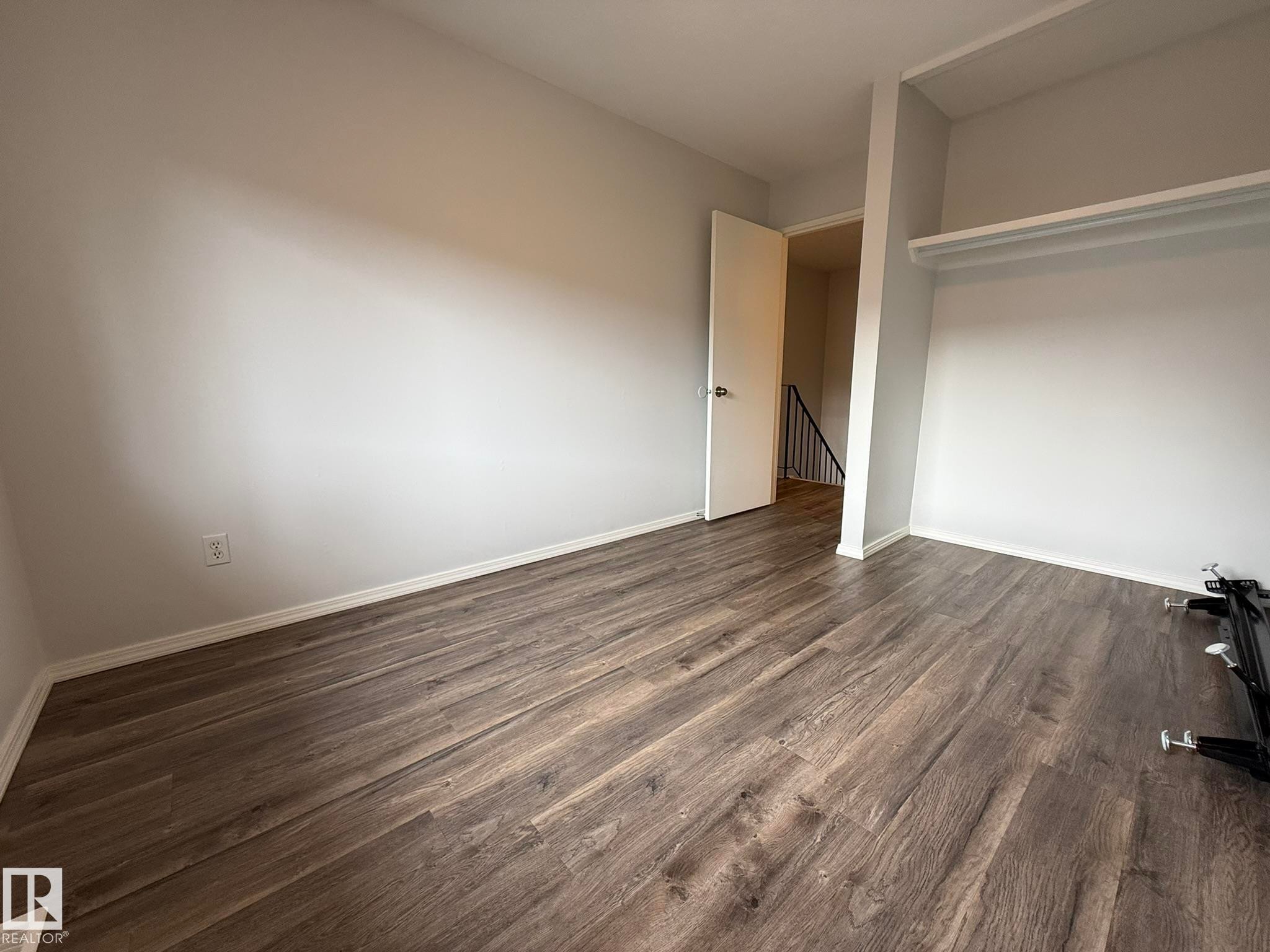 Room featuring wood-finish flooring, light grey painted walls, white trim, and an open closet space with shelving - 166 Roseland Village, Edmonton, AB - Indoor Photo Showing Other Room