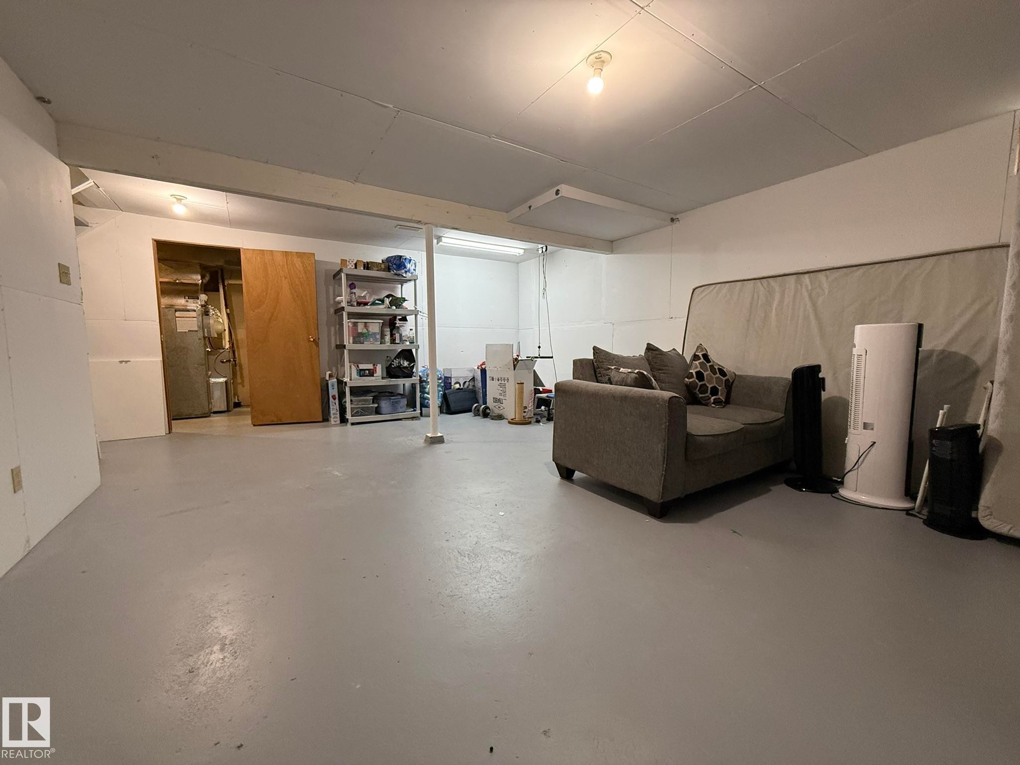 Spacious utility room featuring painted concrete flooring, a support column, and exposed overhead joists - 166 Roseland Village, Edmonton, AB - Indoor