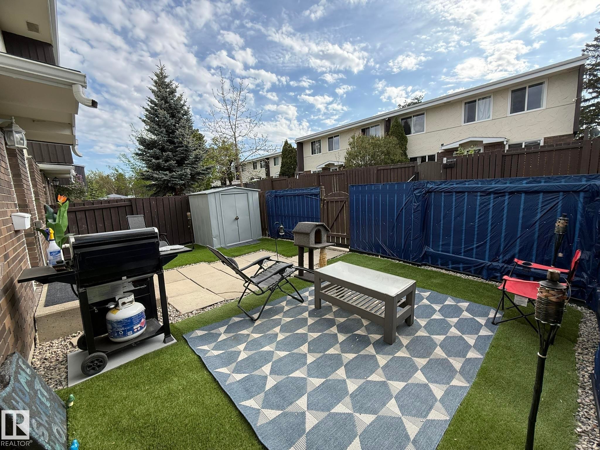 Private outdoor space featuring artificial turf, a concrete patio, and a brown privacy fence - 166 Roseland Village, Edmonton, AB - Outdoor With Exterior