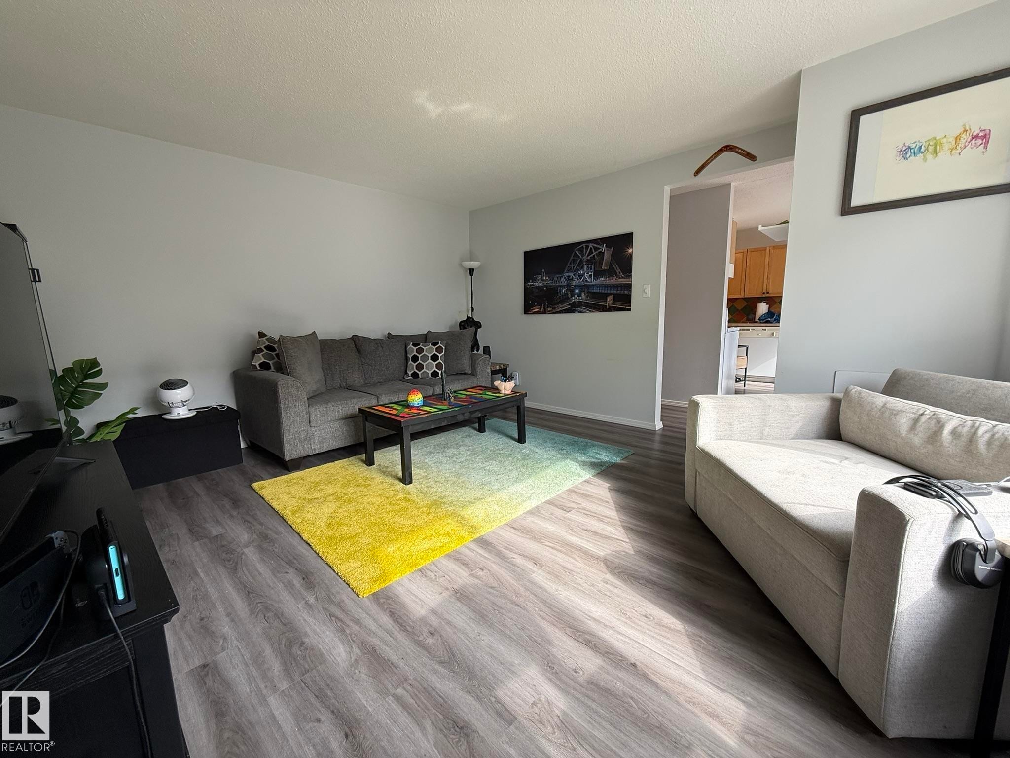 Living area featuring wood-finish flooring, light grey painted walls, and a visible doorway to an additional space - 166 Roseland Village, Edmonton, AB - Indoor Photo Showing Living Room