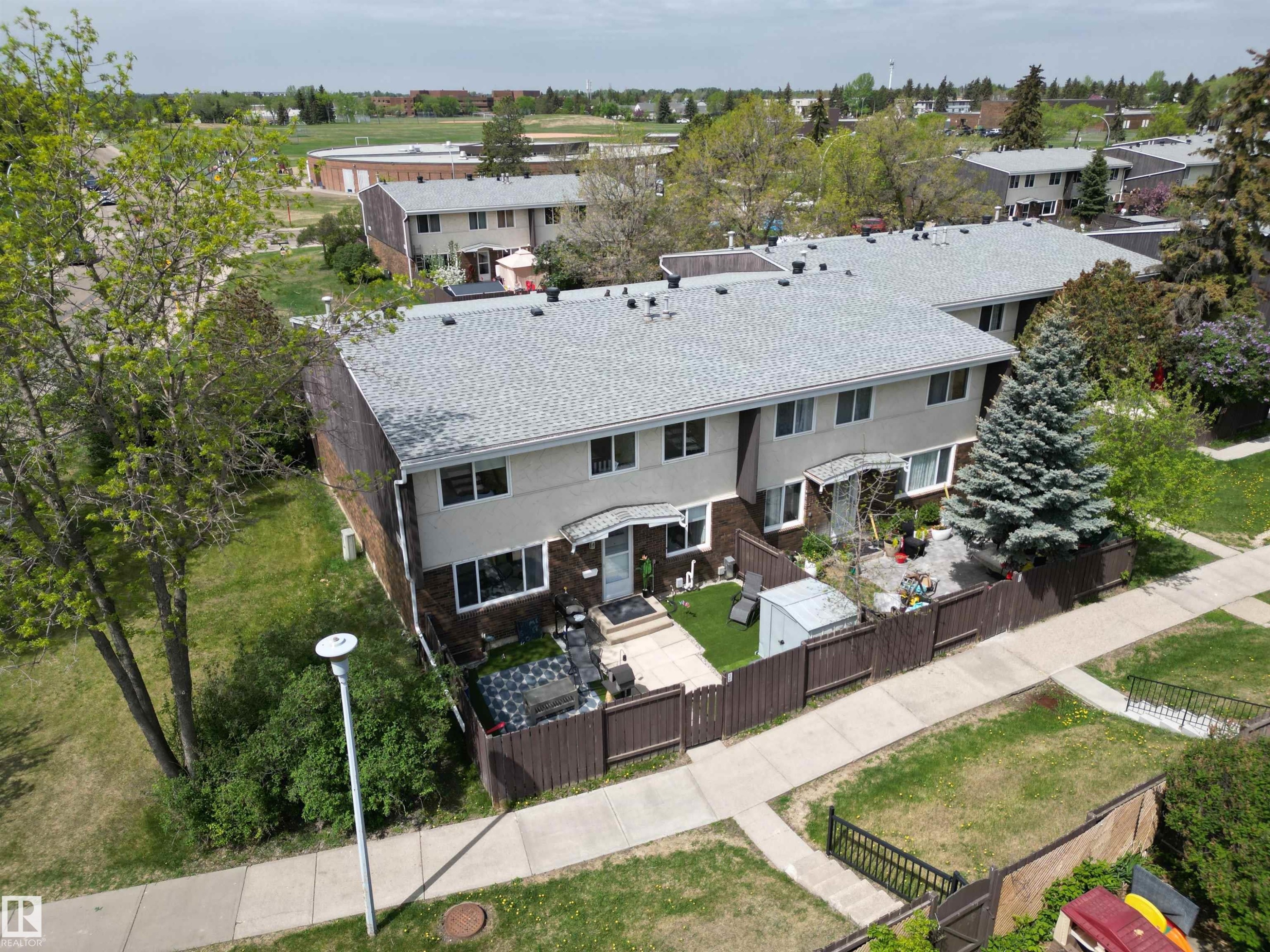Exterior showcasing a grey shingle roof, brick and stucco facade, white-framed windows, and a fenced patio area - 166 Roseland Village, Edmonton, AB - Outdoor