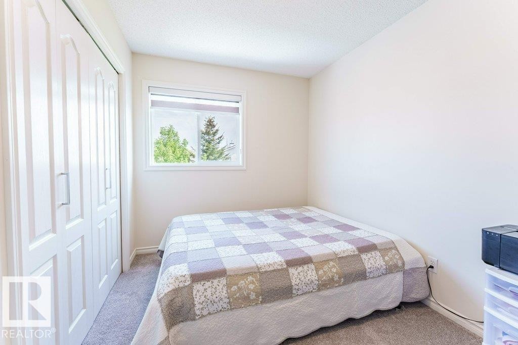 Bedroom featuring neutral-toned carpet, a white framed window with roller shade, and bi-fold closet doors - 3525 22 Street, Edmonton, AB - Indoor Photo Showing Bedroom