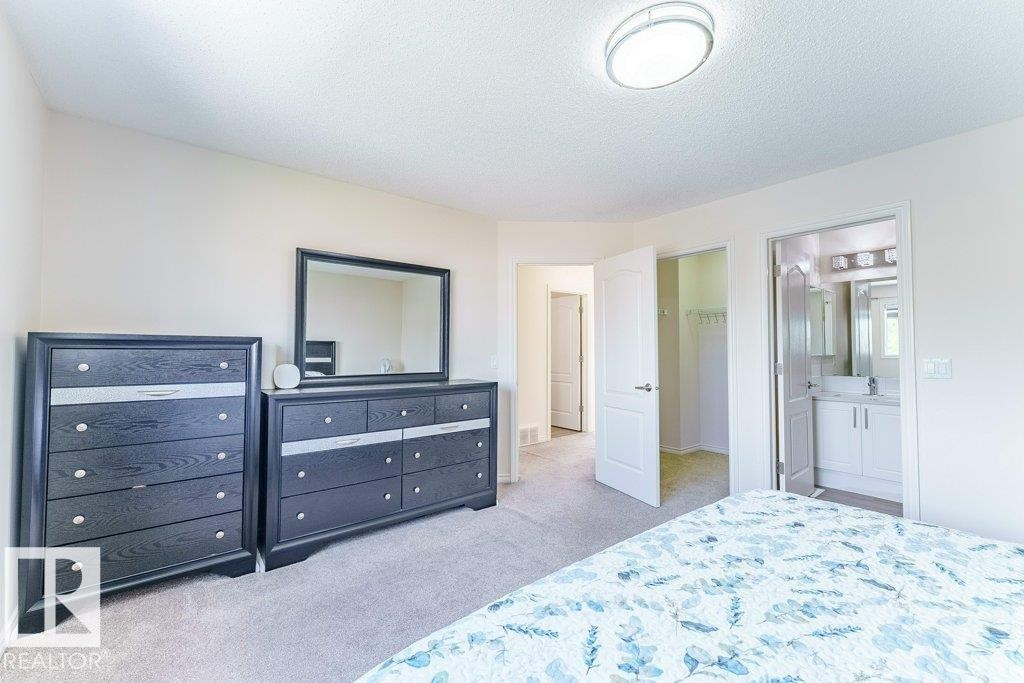 Bedroom featuring plush carpet, warm neutral wall tones, a ceiling-mounted light fixture, and an open doorway to a bathroom with a white vanity and mirror - 3525 22 Street, Edmonton, AB - Indoor Photo Showing Bedroom