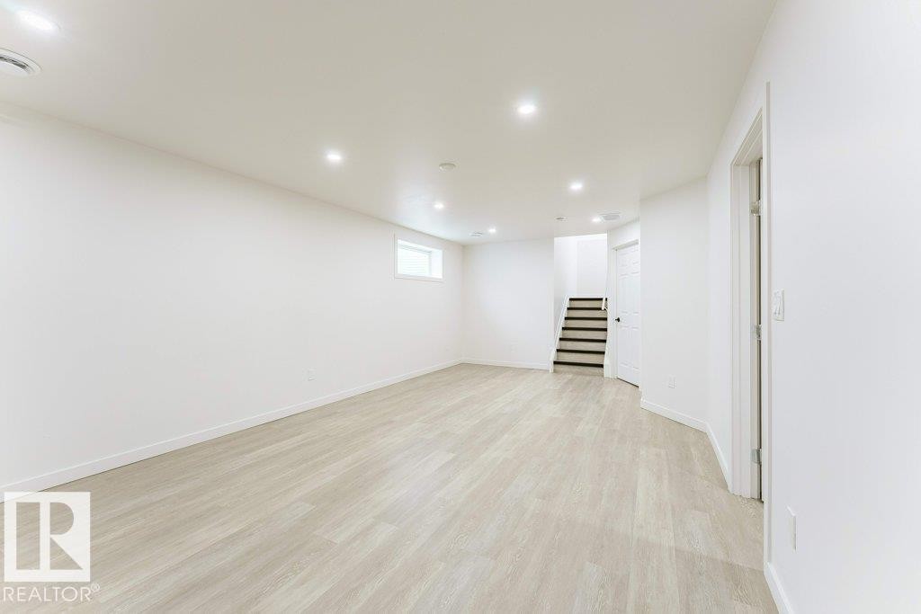 Spacious room featuring light wood-finish flooring, recessed lighting, white walls, and a window for natural illumination - 3525 22 Street, Edmonton, AB - Indoor