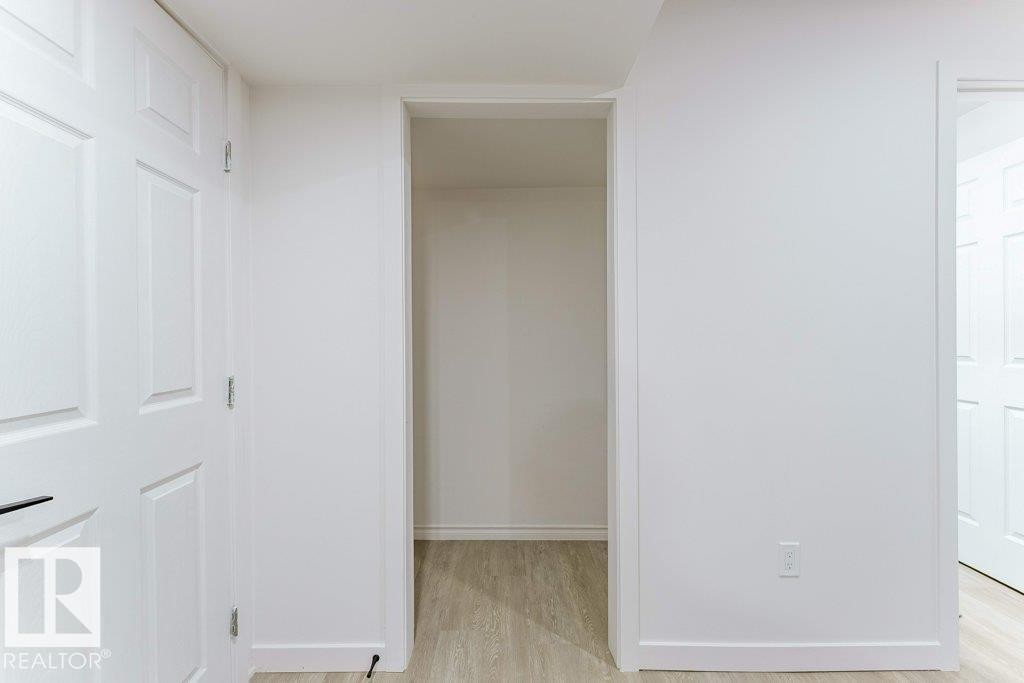 Interior hallway featuring light wood-finish flooring, crisp white walls, and bright white paneled doors with black hardware - 3525 22 Street, Edmonton, AB - Indoor Photo Showing Other Room