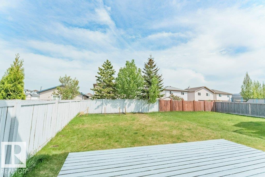 Spacious backyard featuring a white painted wooden fence, diverse mature trees, and a wooden deck area - 3525 22 Street, Edmonton, AB - Outdoor With Backyard