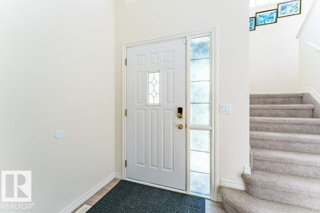 Entryway featuring a paneled door with decorative glass inserts and an adjacent stained-glass sidelight, a smart door lock, and a carpeted staircase with a white railing - 3525 22 Street, Edmonton, AB - Indoor Photo Showing Other Room