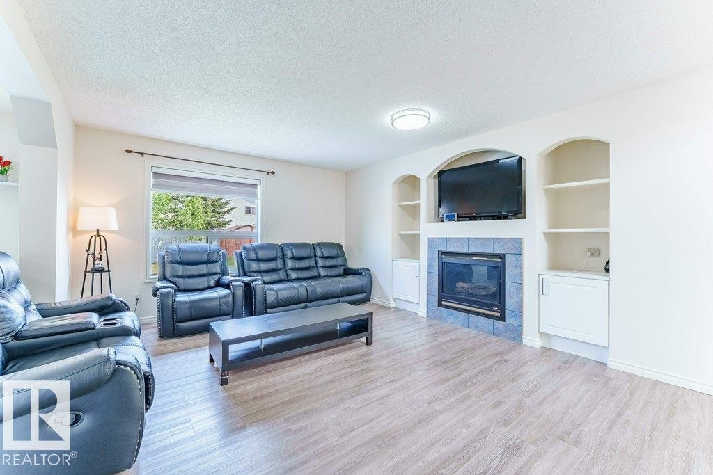 Living room featuring wood-finish flooring, a fireplace with blue tile surround, and integrated shelving with lower cabinetry - 3525 22 Street, Edmonton, AB - Indoor Photo Showing Living Room With Fireplace