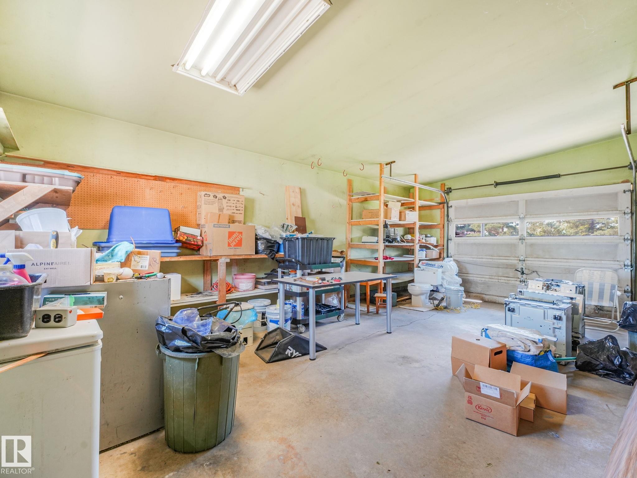 Spacious garage featuring a concrete floor, overhead fluorescent lighting, and a paneled garage door with upper window inserts - 15011 72A Street, Edmonton, AB