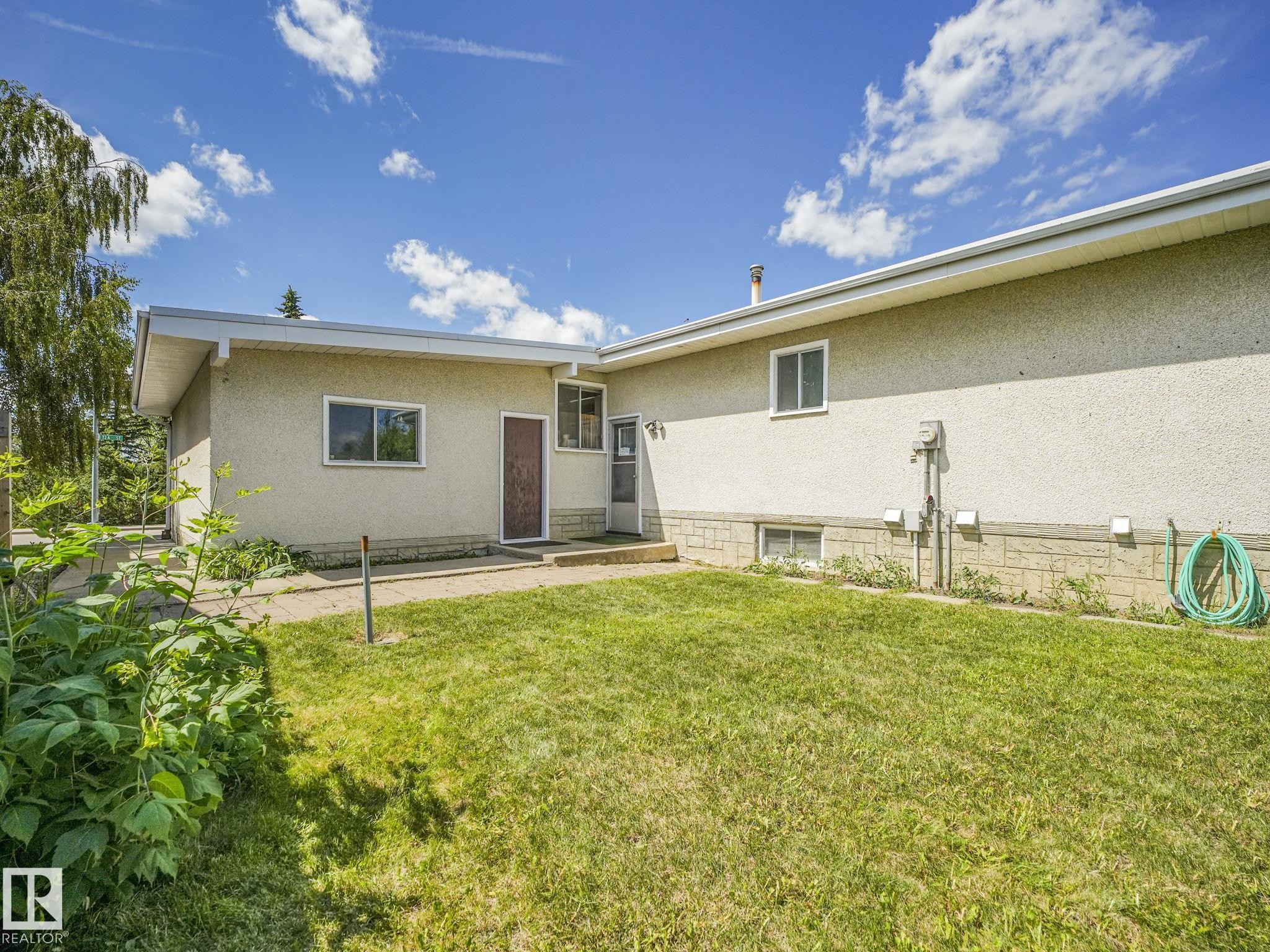 Expansive grassy yard area with a stucco exterior, concrete foundation accents, and multiple windows - 15011 72A Street, Edmonton, AB