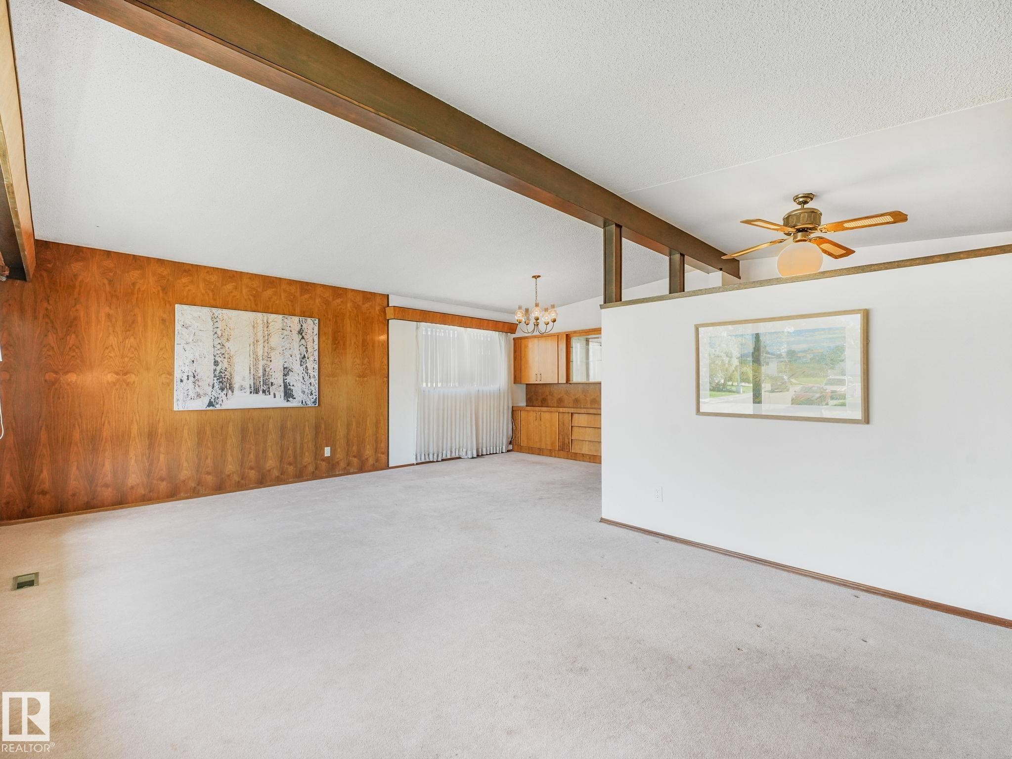 Spacious room featuring a vaulted ceiling with exposed wood beams, a wood-paneled accent wall, and light-toned carpeting - 15011 72A Street, Edmonton, AB