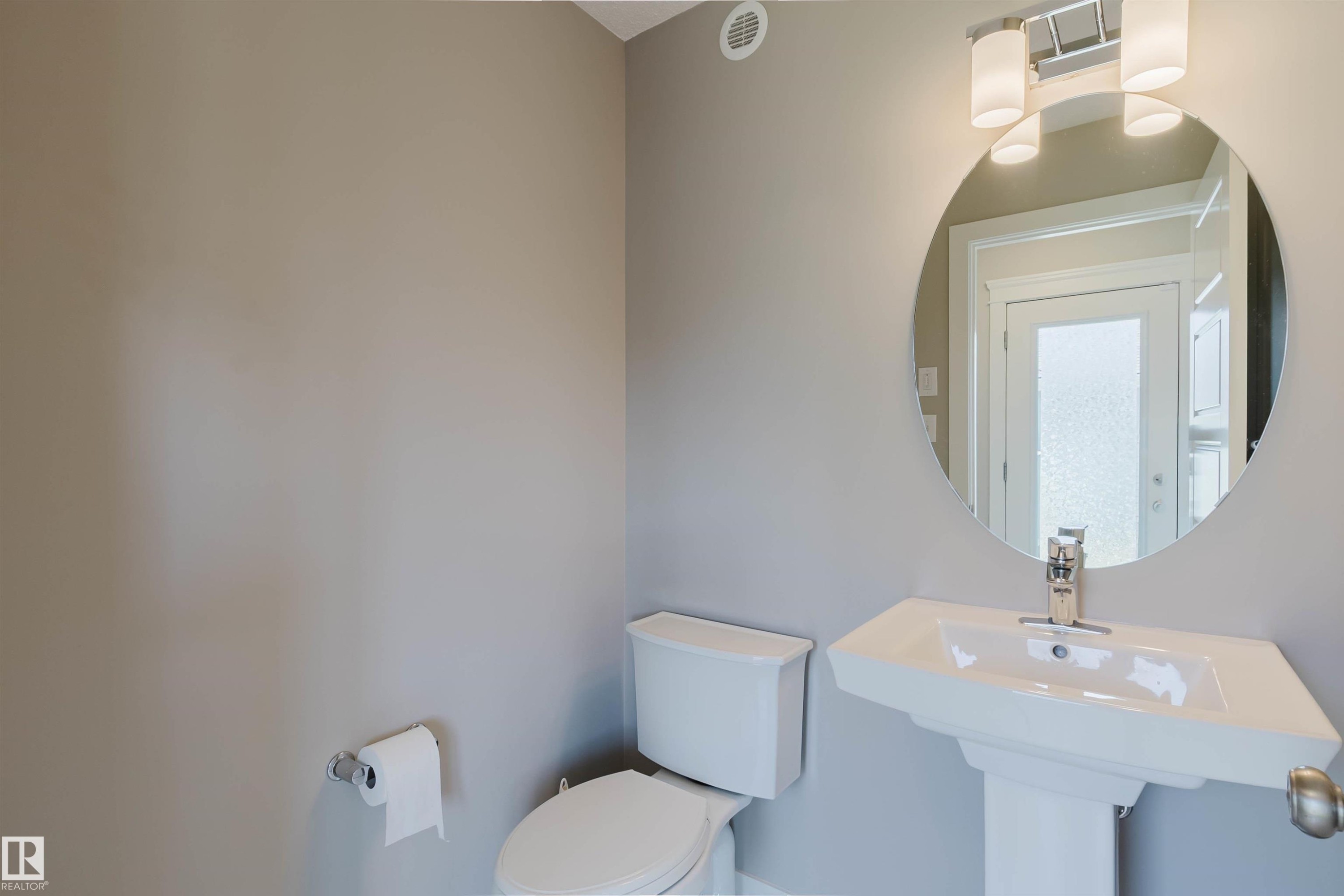 Pedestal sink with chrome faucet, circular mirror, and modern vanity lighting - 2472 Glenridding Boulevard, Edmonton, AB
