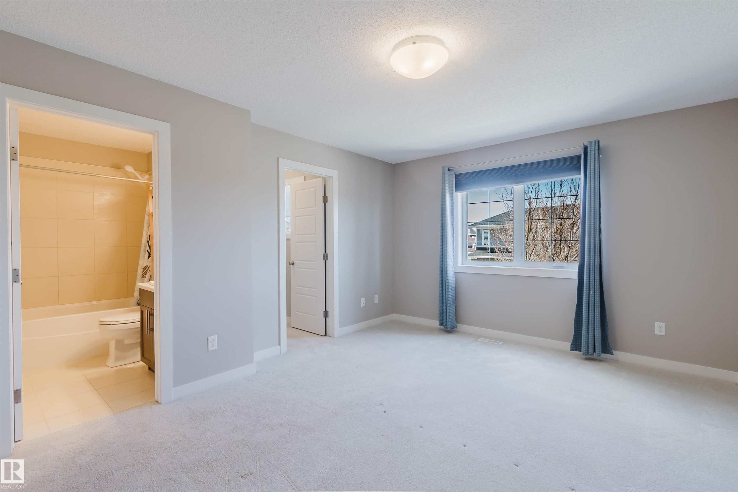 Carpeted room featuring a window with blue drapes, an overhead light fixture, and two doorways - 2472 Glenridding Boulevard, Edmonton, AB