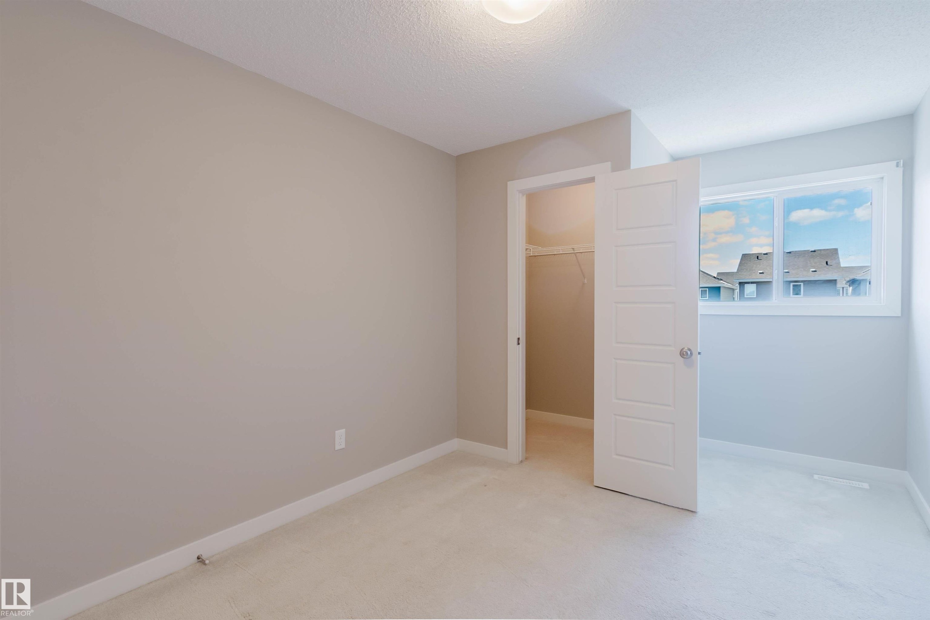 Neutral-toned interior room featuring light carpet flooring, a walk-in closet with built-in shelving, and a window with white trim - 2472 Glenridding Boulevard, Edmonton, AB