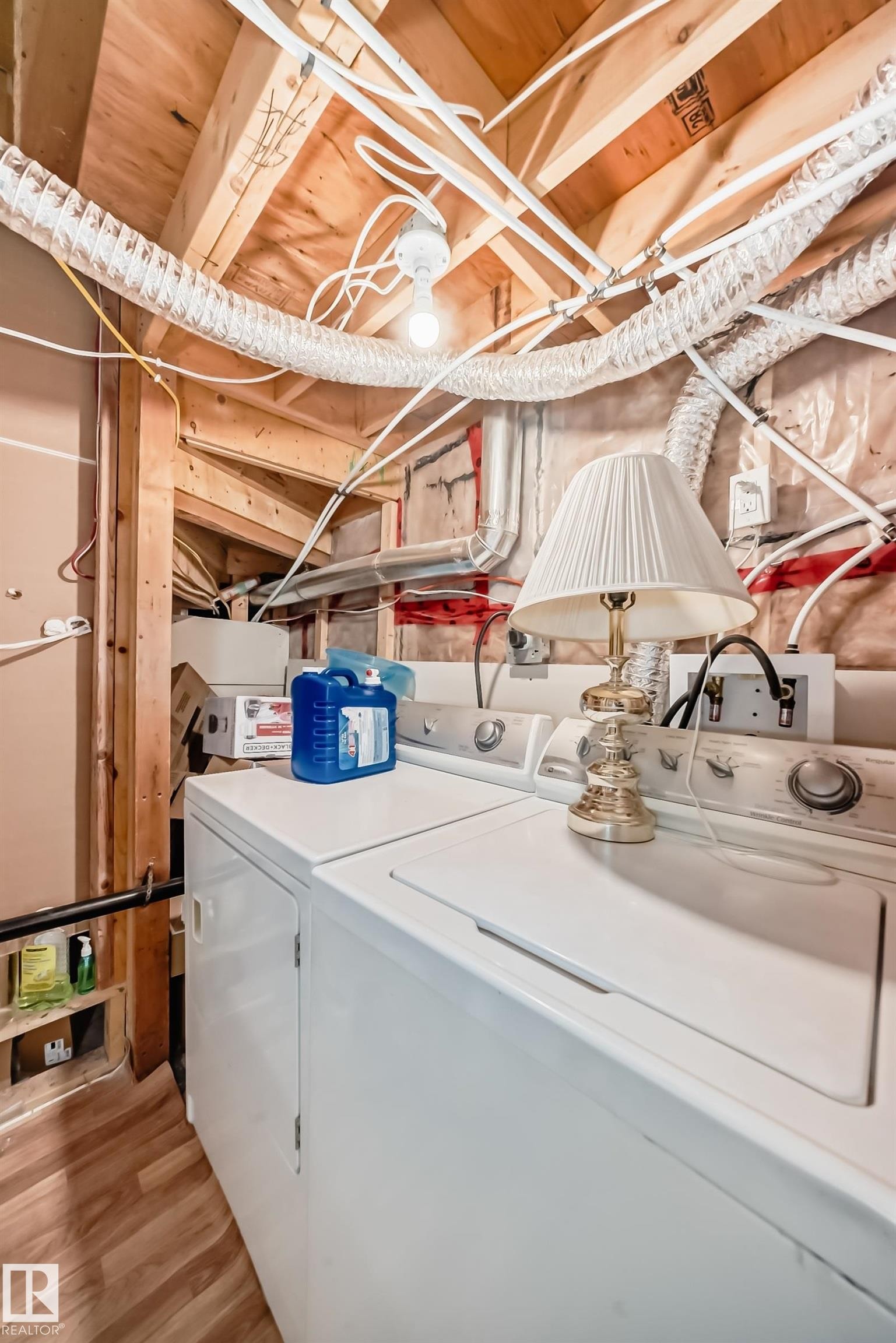 Laundry area featuring a top-load washing machine, a front-load dryer, exposed wood ceiling joists, and wood-finish flooring - #2 12042 101 St Nw, Edmonton, AB - Indoor Photo Showing Laundry Room