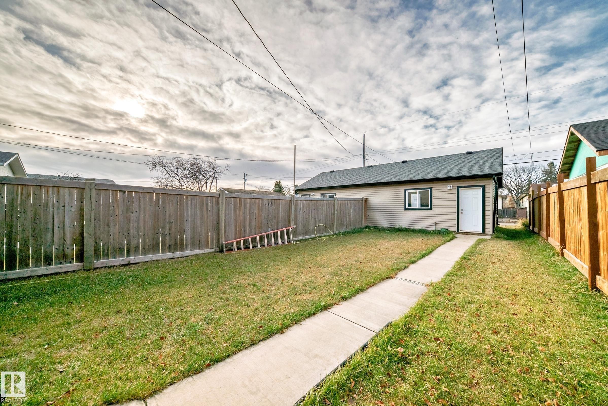 Rear accessory building with a single white door and a small window, set against a backdrop of a fenced yard - #2 12042 101 St Nw, Edmonton, AB - Outdoor