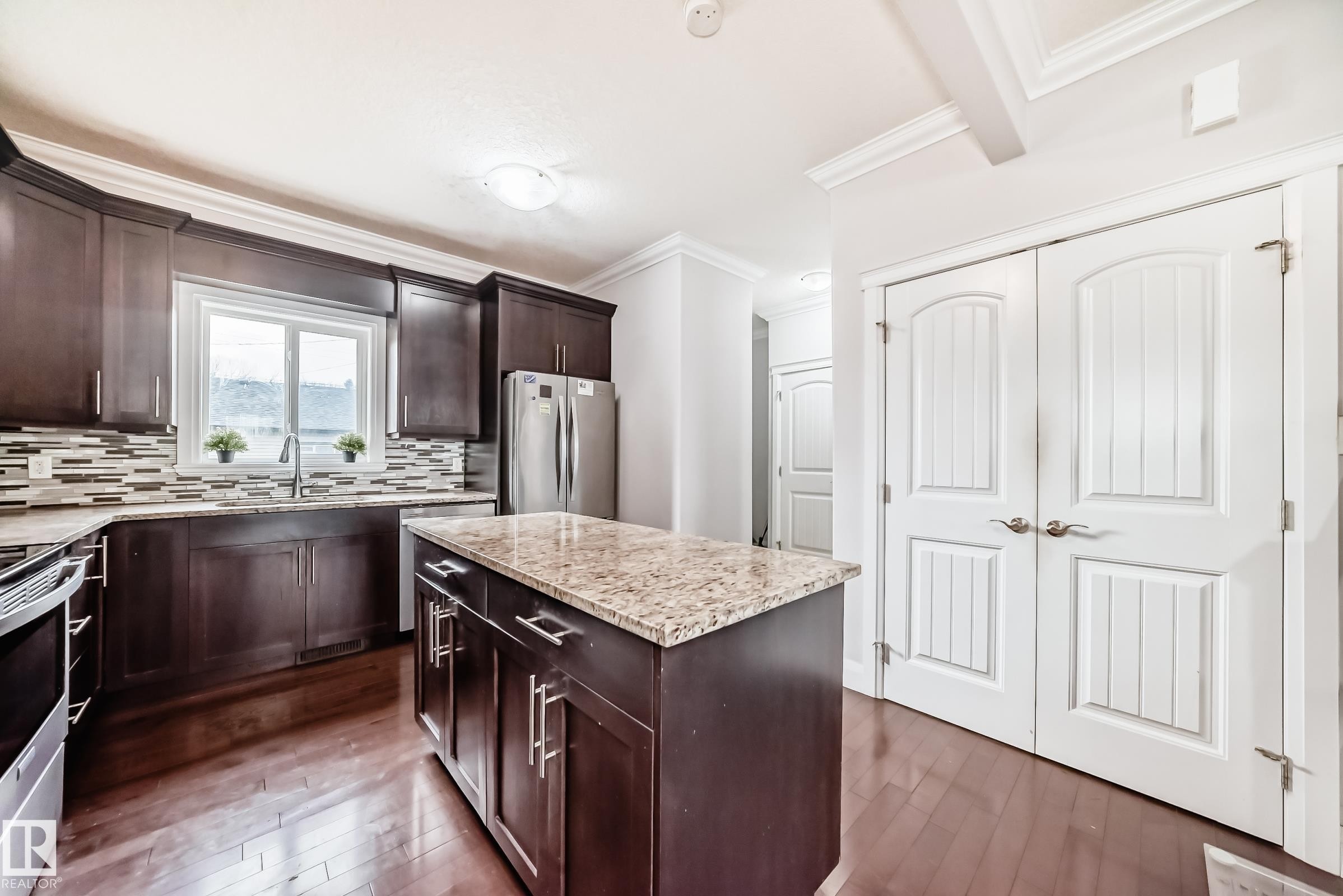 Kitchen featuring dark wood cabinetry, a central island with a light-toned countertop, and stainless steel appliances - #2 12042 101 St Nw, Edmonton, AB - Indoor Photo Showing Kitchen With Double Sink With Upgraded Kitchen