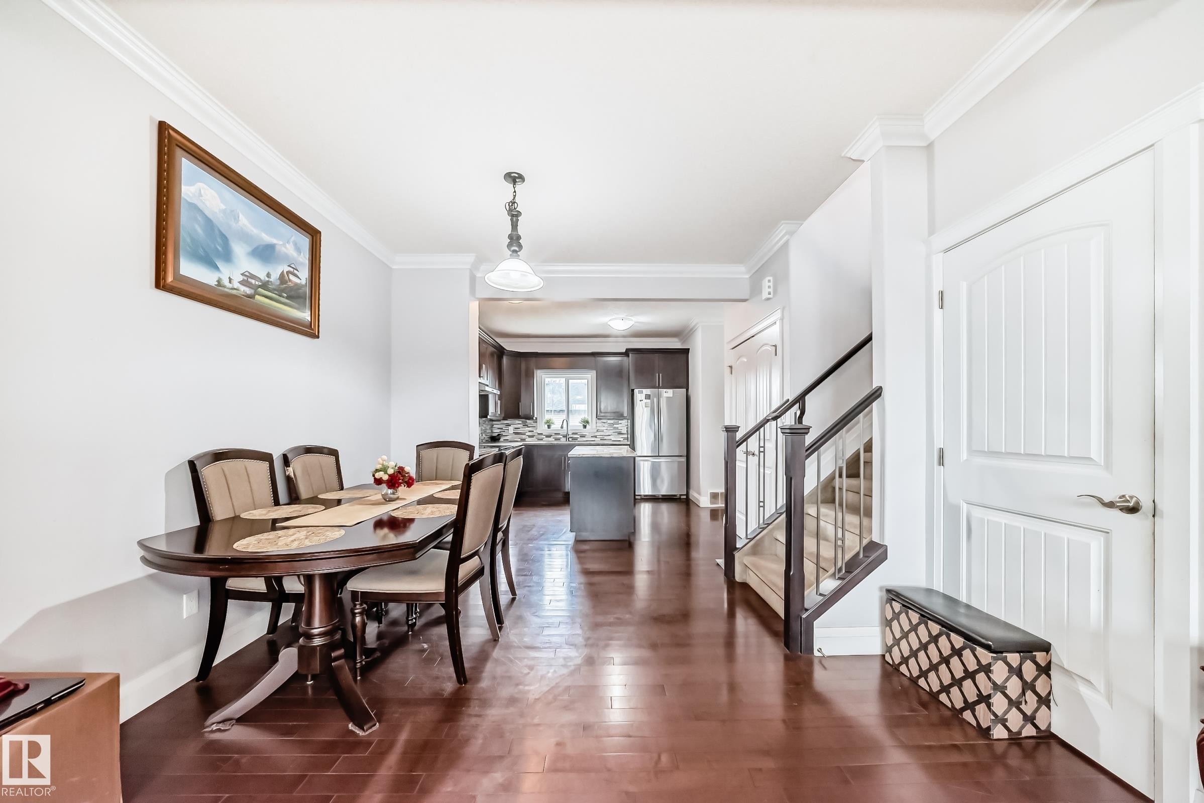 Hardwood-finish flooring extending throughout the dining area, featuring crown molding, an open concept layout, and a staircase with dark wood newel posts and handrail - #2 12042 101 St Nw, Edmonton, AB - Indoor Photo Showing Dining Room