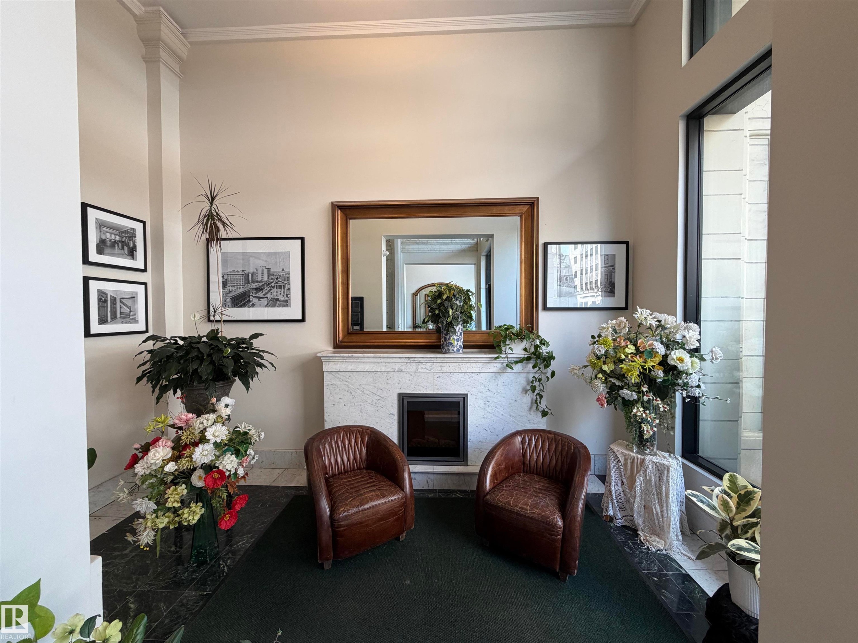 Foyer showcasing a white marble-clad fireplace with dark insert, flanked by two brown leather barrel chairs - #210 10134 100 St Nw, Edmonton, AB - Indoor Photo Showing Other Room With Fireplace