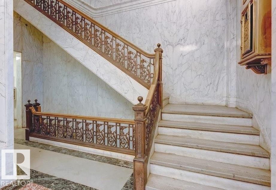 Grand staircase featuring a dark wood handrail with intricate metal balusters - #210 10134 100 St Nw, Edmonton, AB - Indoor Photo Showing Other Room