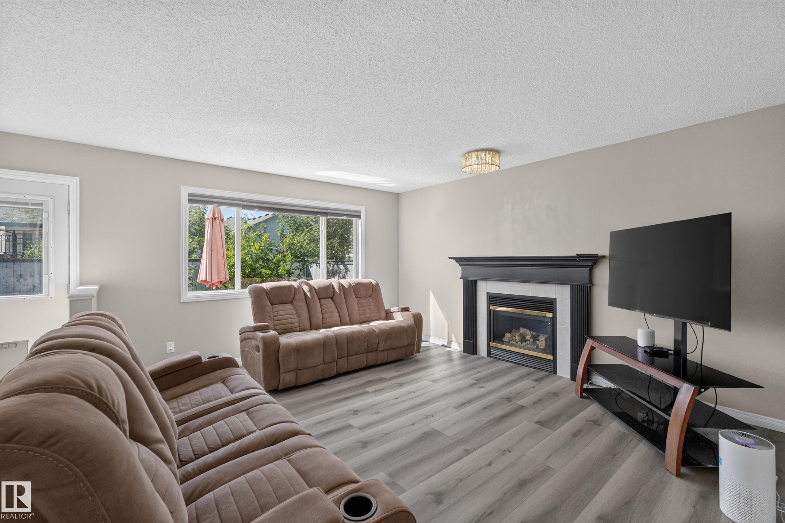 Living area featuring light-toned walls, wood-finish flooring, and a fireplace with a black mantel and white surround - 2327 37B Avenue, Edmonton, AB
