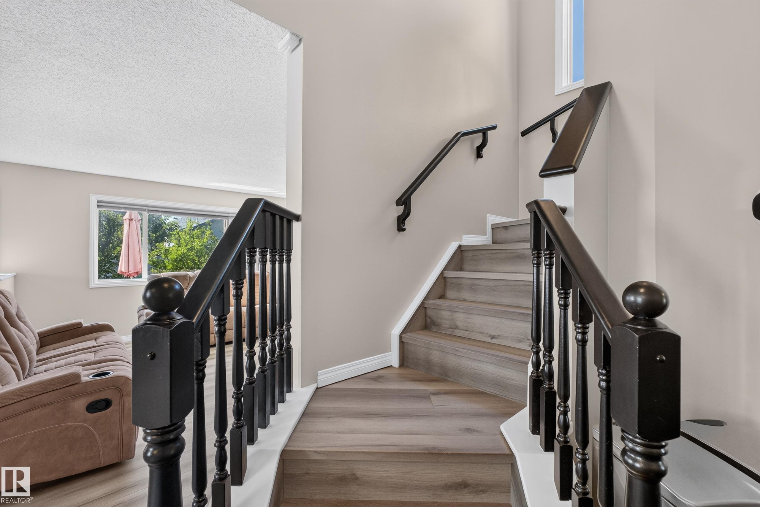 Staircase featuring dark wood banisters and balusters, light wood-finish treads, and neutral wall paint - 2327 37B Avenue, Edmonton, AB