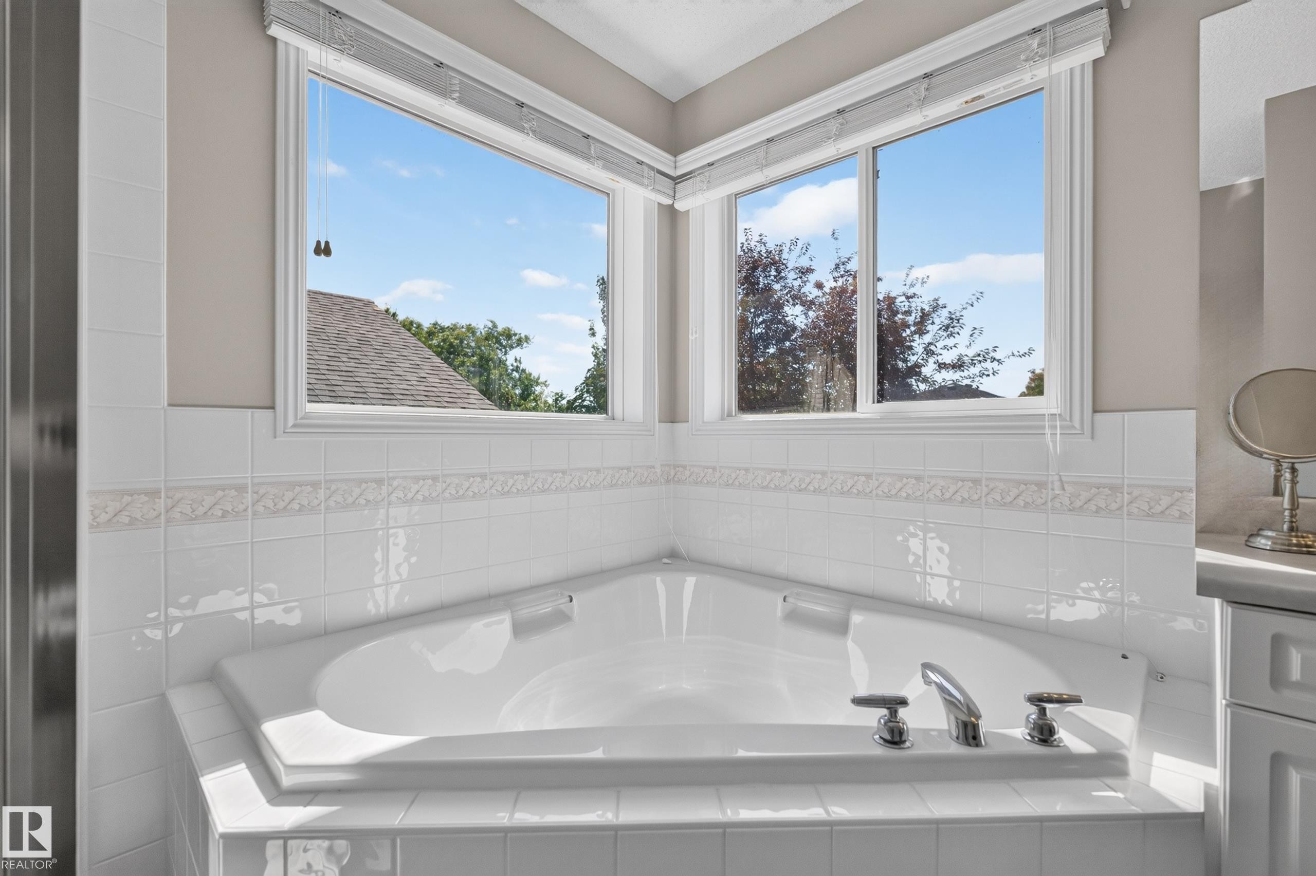 Corner soaking tub with polished chrome fixtures, surrounded by white ceramic wall tile - 2327 37B Avenue, Edmonton, AB