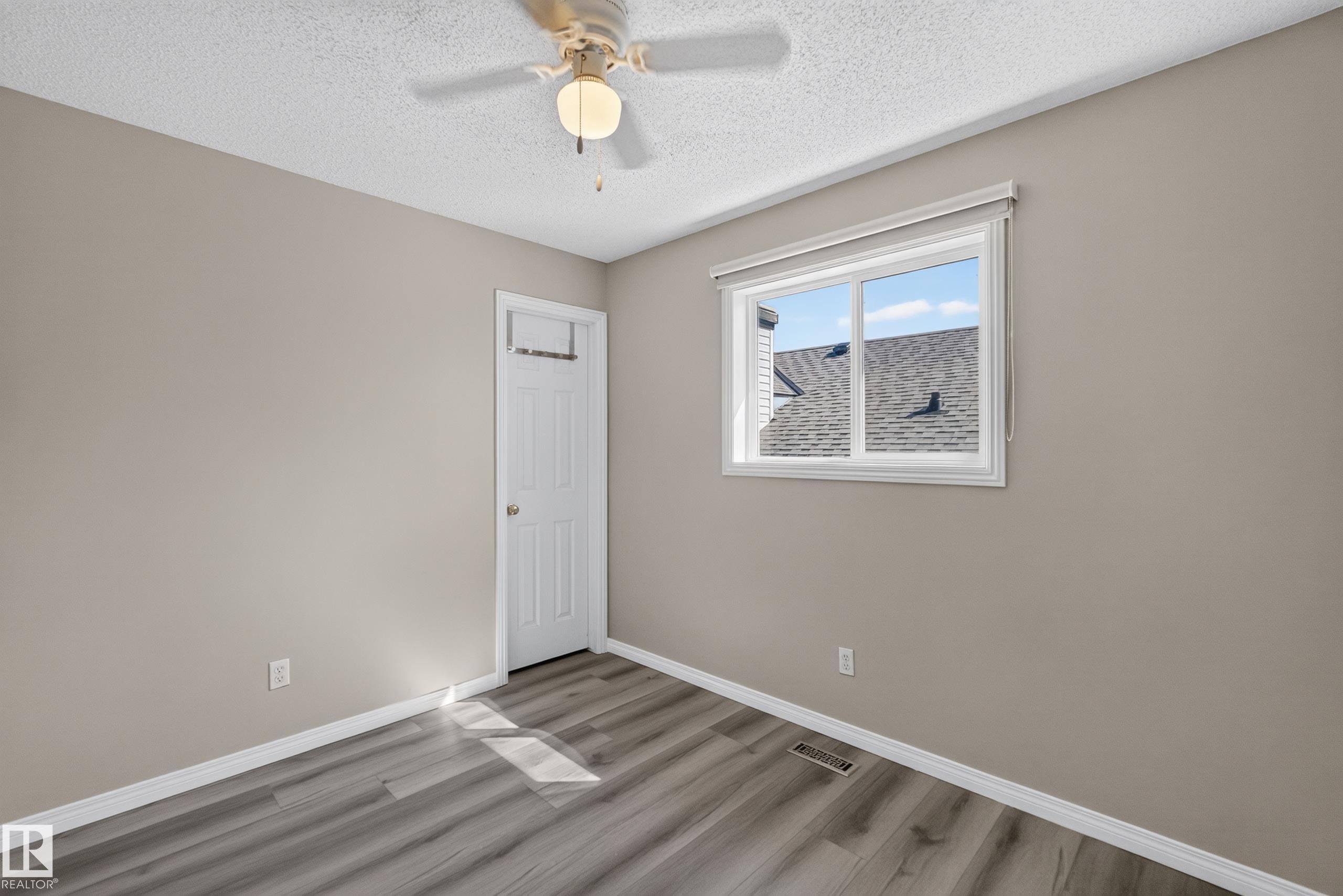 Neutral-toned room featuring a ceiling fan with integrated lighting, wood-finish flooring, a white trim package, and a white window with a roller blind - 2327 37B Avenue, Edmonton, AB