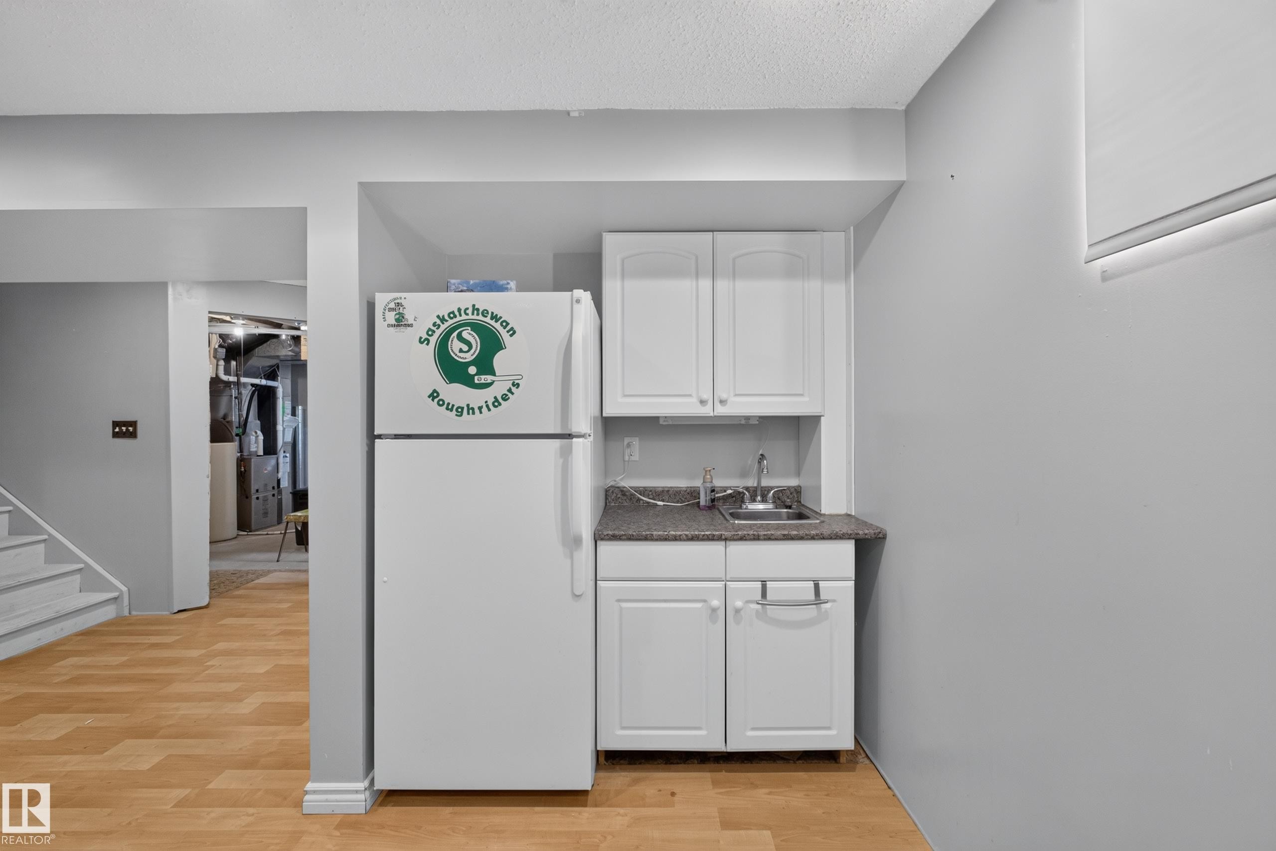 Compact kitchen area featuring white cabinetry, a built-in stainless steel sink, and a speckled countertop - 2327 37B Avenue, Edmonton, AB