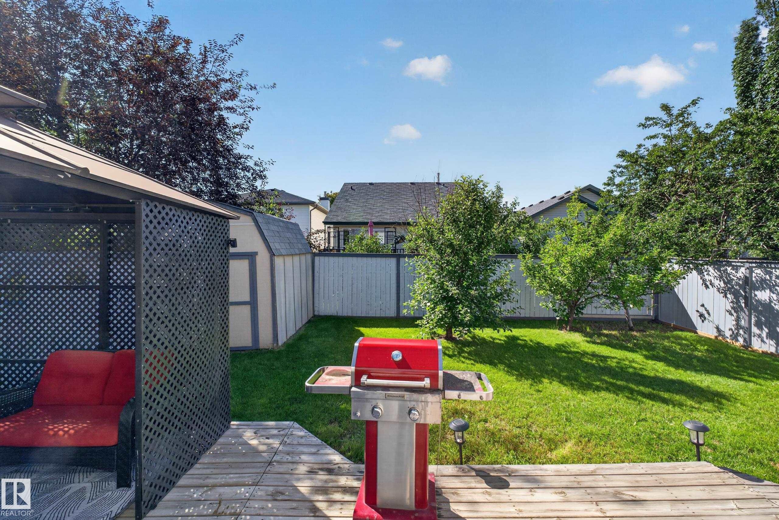 Expansive backyard featuring a wooden deck, a built-in gazebo with lattice screening, a detached storage shed, a green lawn, and mature trees - 2327 37B Avenue, Edmonton, AB