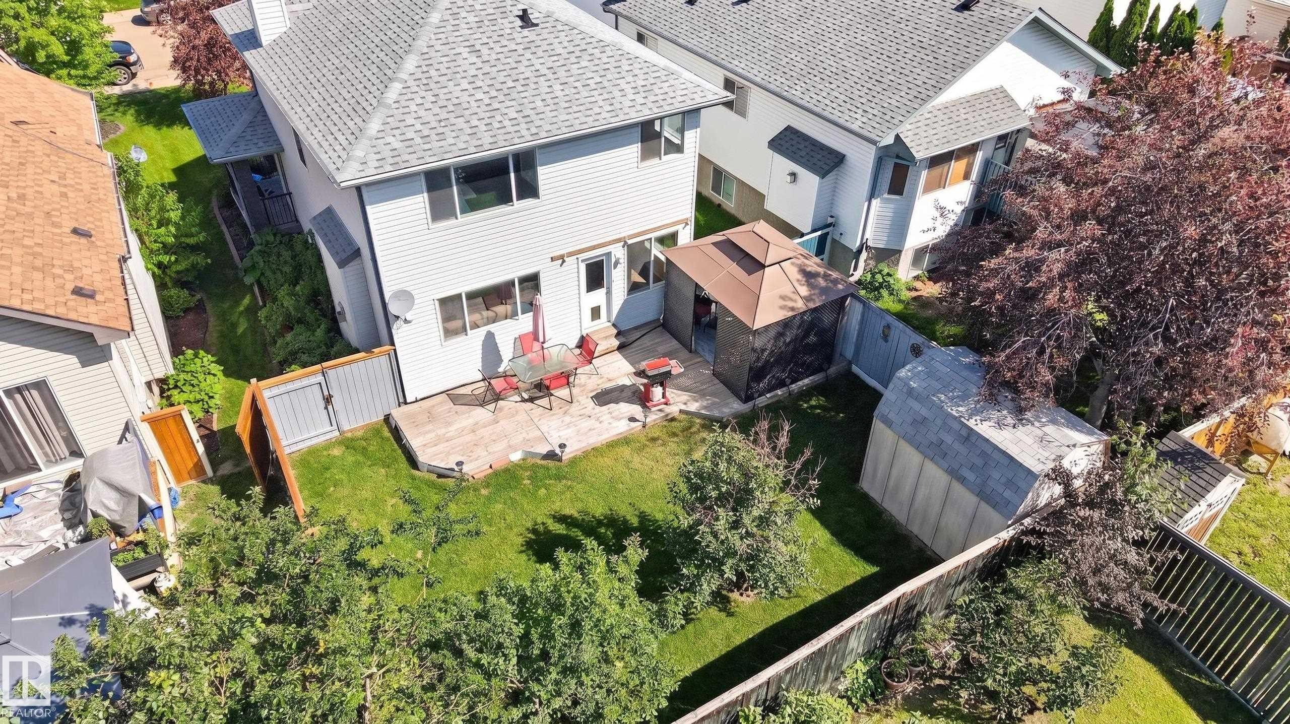 Spacious backyard featuring a concrete patio, a detached storage shed, perimeter fencing, and mature trees - 2327 37B Avenue, Edmonton, AB