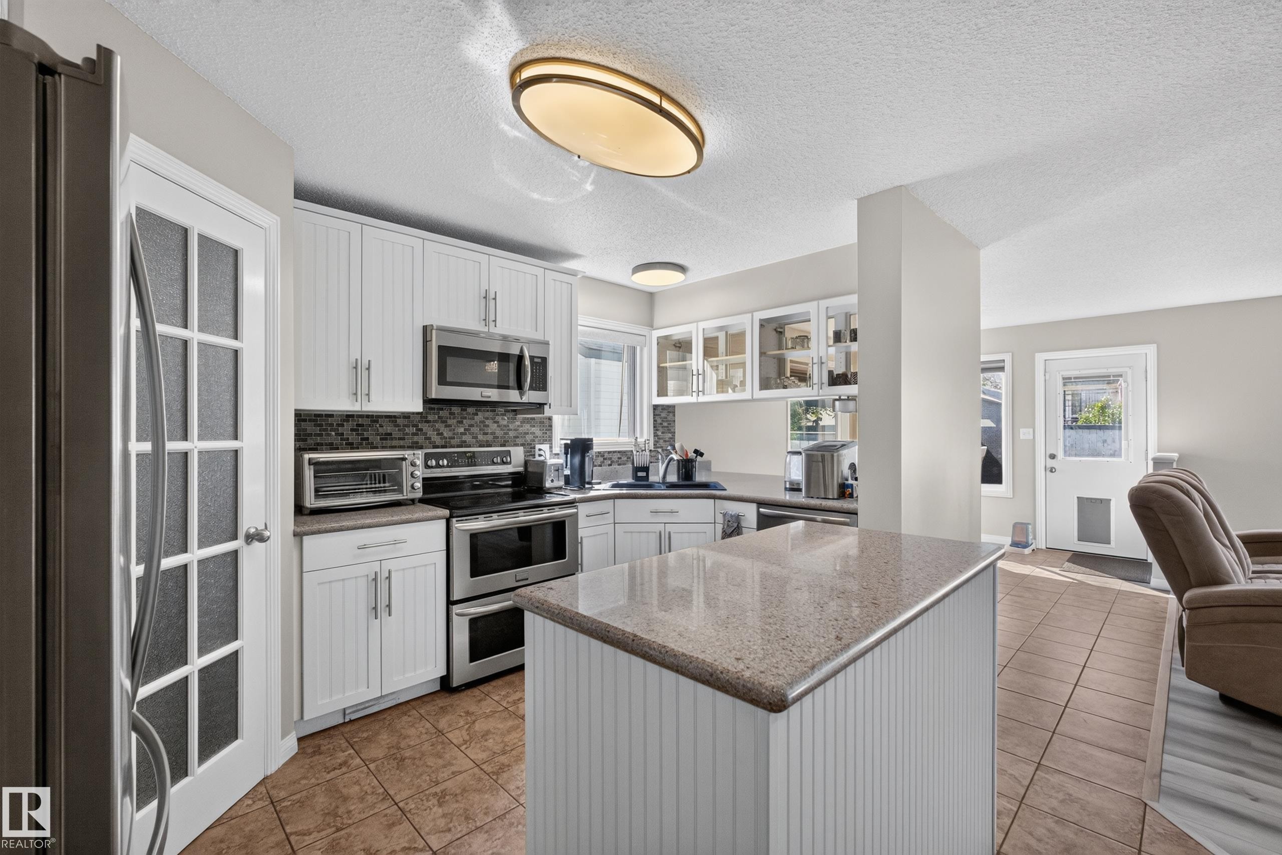 Kitchen featuring white cabinetry, stainless steel appliances, a stone-finish countertop island, and tile flooring - 2327 37B Avenue, Edmonton, AB
