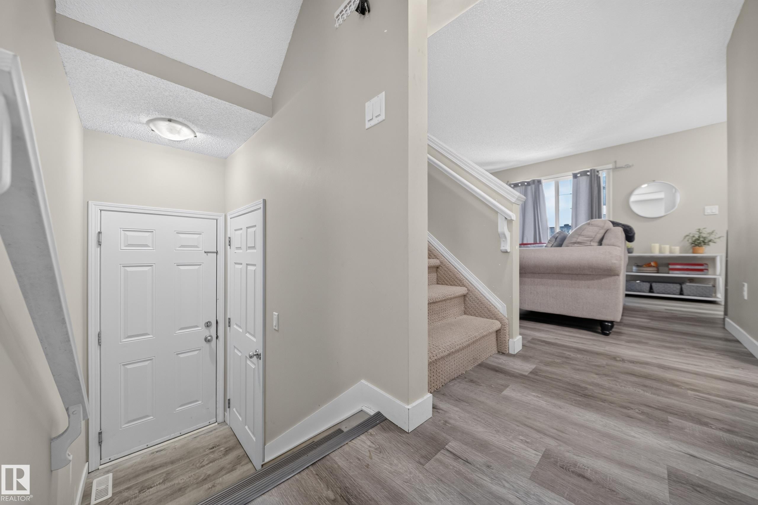 Entry foyer featuring a white paneled door, vaulted ceiling, and wood-finish flooring - 59 2503 24 Street, Edmonton, AB