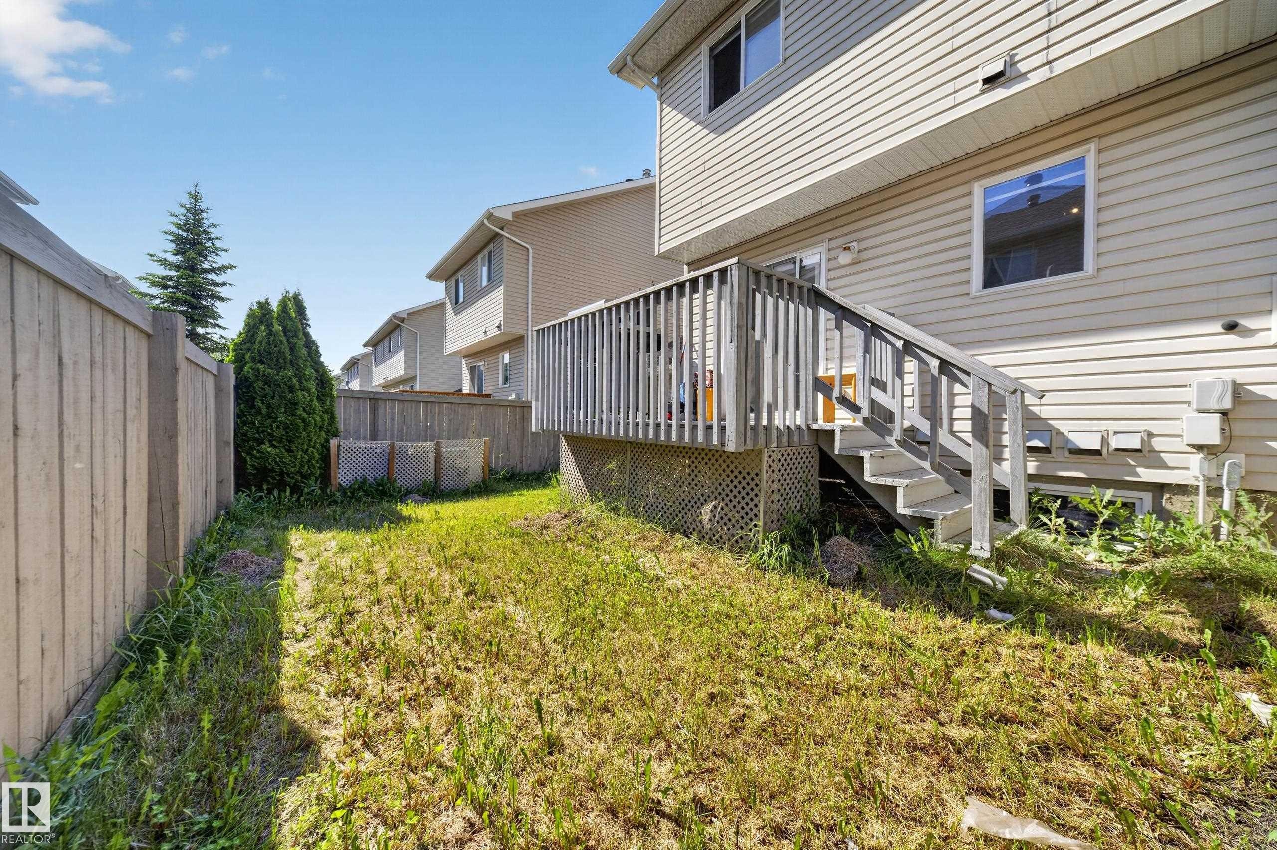 Rear yard featuring a wooden deck with railing and stairs, vinyl siding, and a privacy fence - 59 2503 24 Street, Edmonton, AB