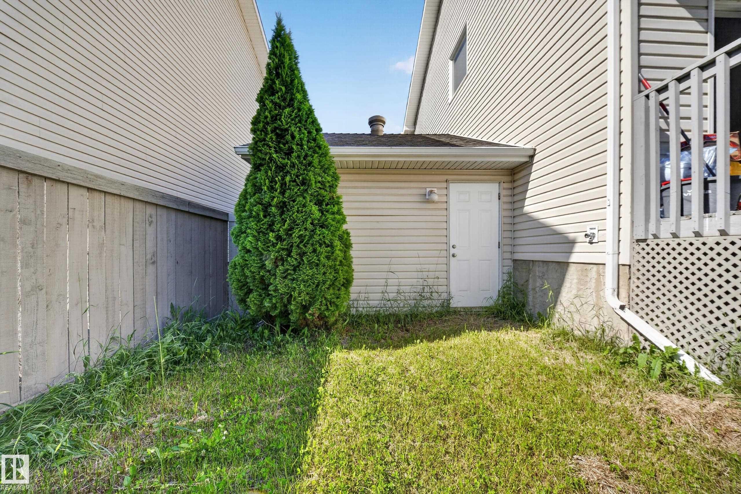 Side yard with a privacy fence, evergreen tree, and building access door - 59 2503 24 Street, Edmonton, AB