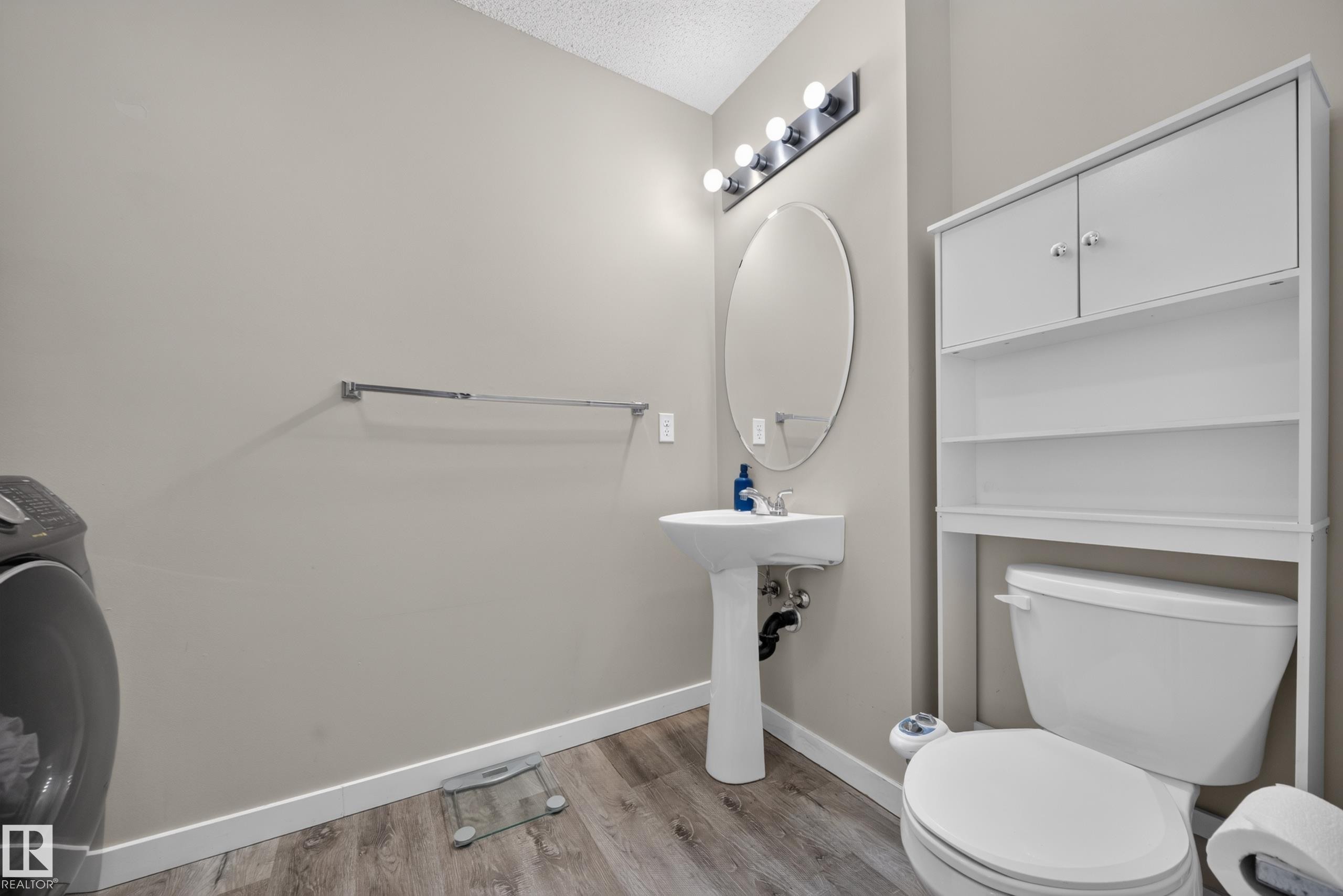 Pedestal sink with an oval mirror and a four-bulb vanity light fixture - 59 2503 24 Street, Edmonton, AB