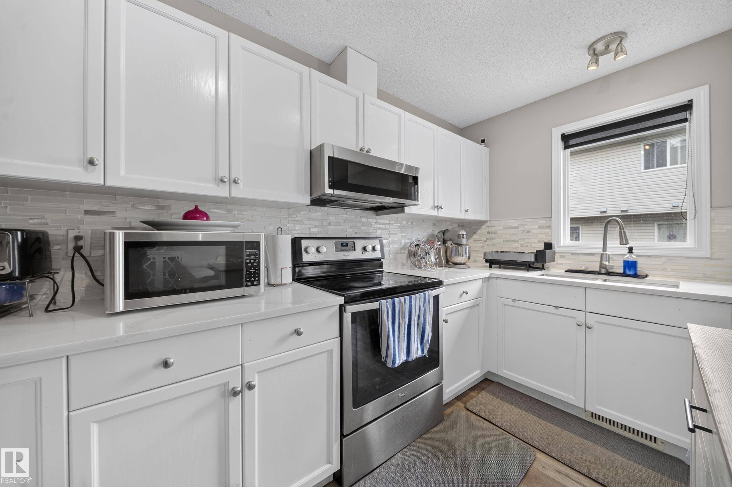 Contemporary kitchen featuring white cabinetry, light countertops, and a full suite of stainless steel appliances - 59 2503 24 Street, Edmonton, AB
