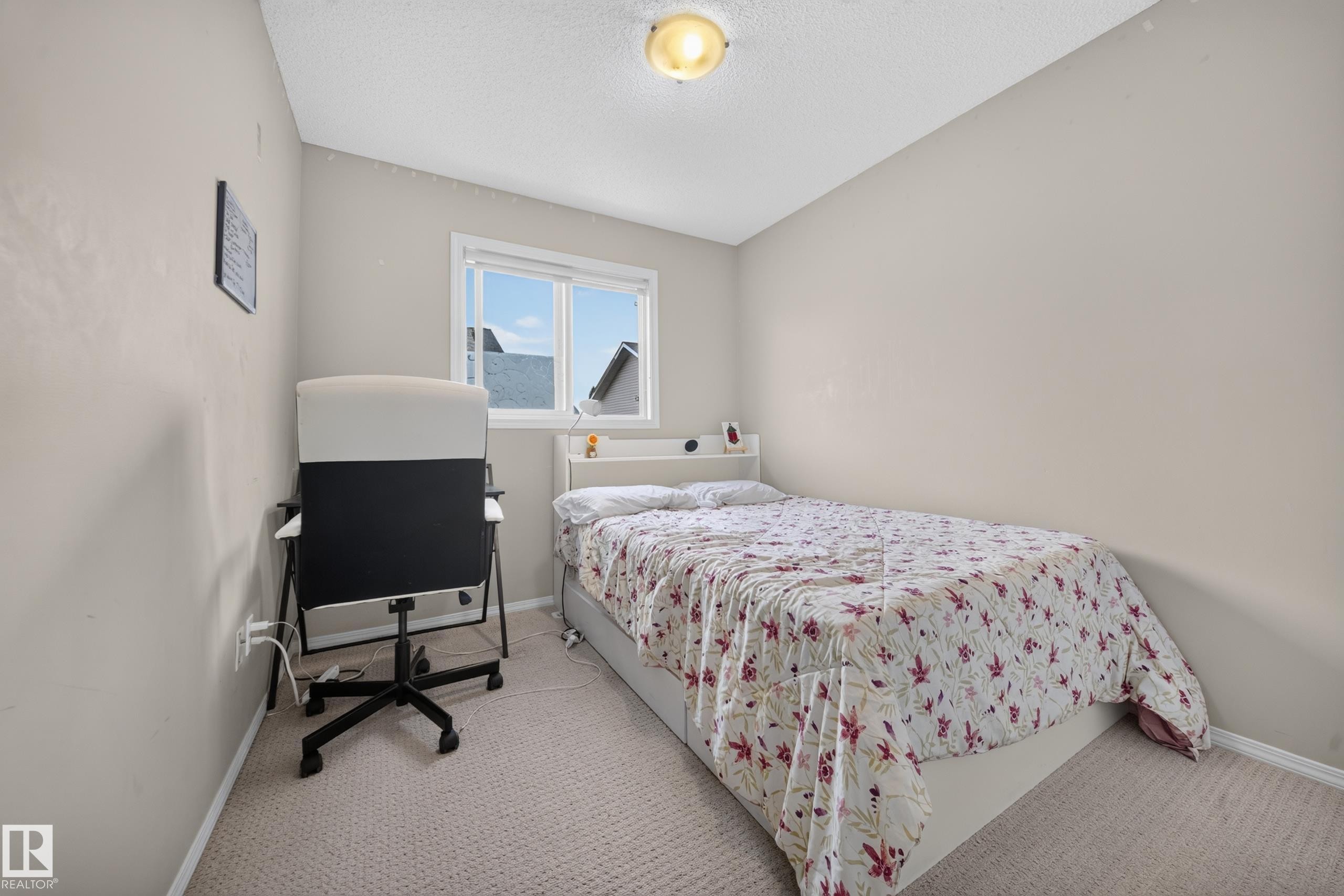 Room featuring neutral wall tones, carpet flooring, a window with exterior residential structures visible, and an overhead flush-mount light fixture - 59 2503 24 Street, Edmonton, AB