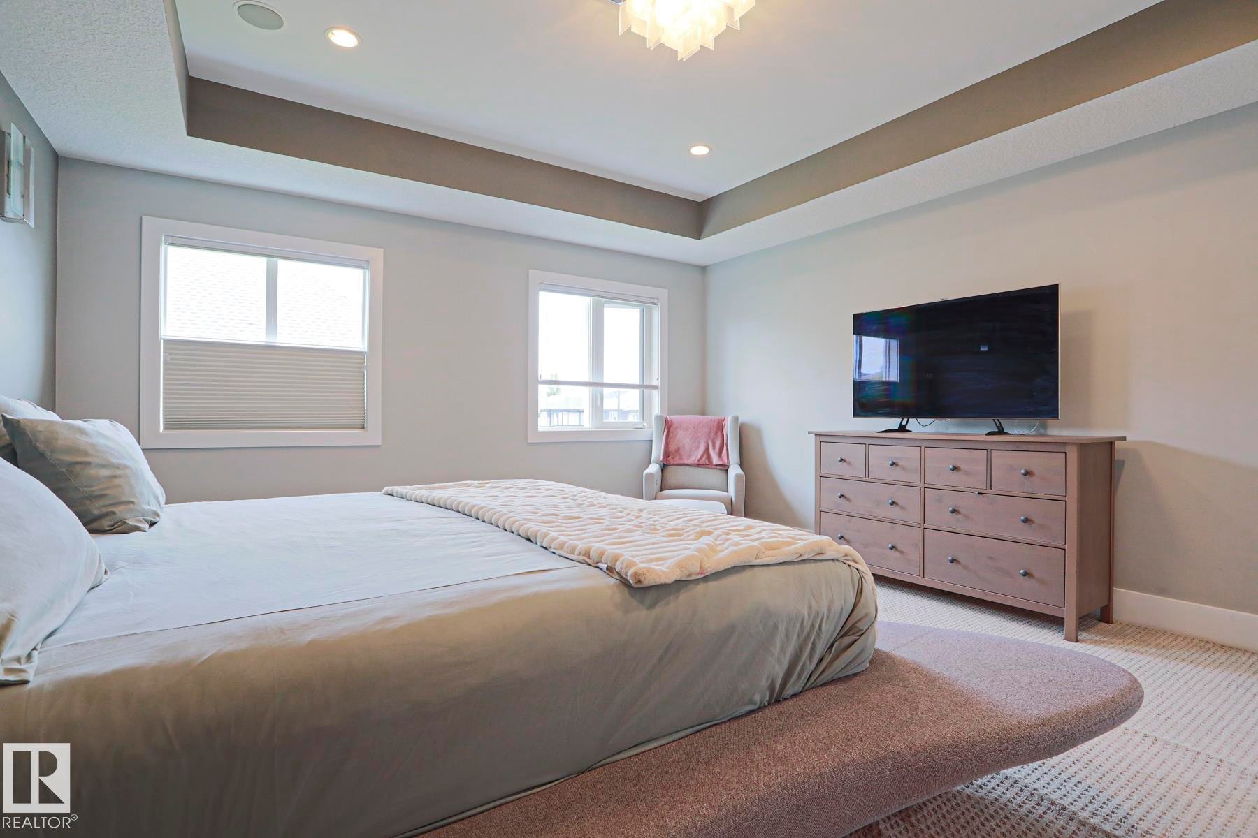 Recessed lighting, tray ceiling, two windows with blinds, and light-colored carpeting - 1304 Ainslie Wynd Sw, Edmonton, AB - Indoor Photo Showing Bedroom