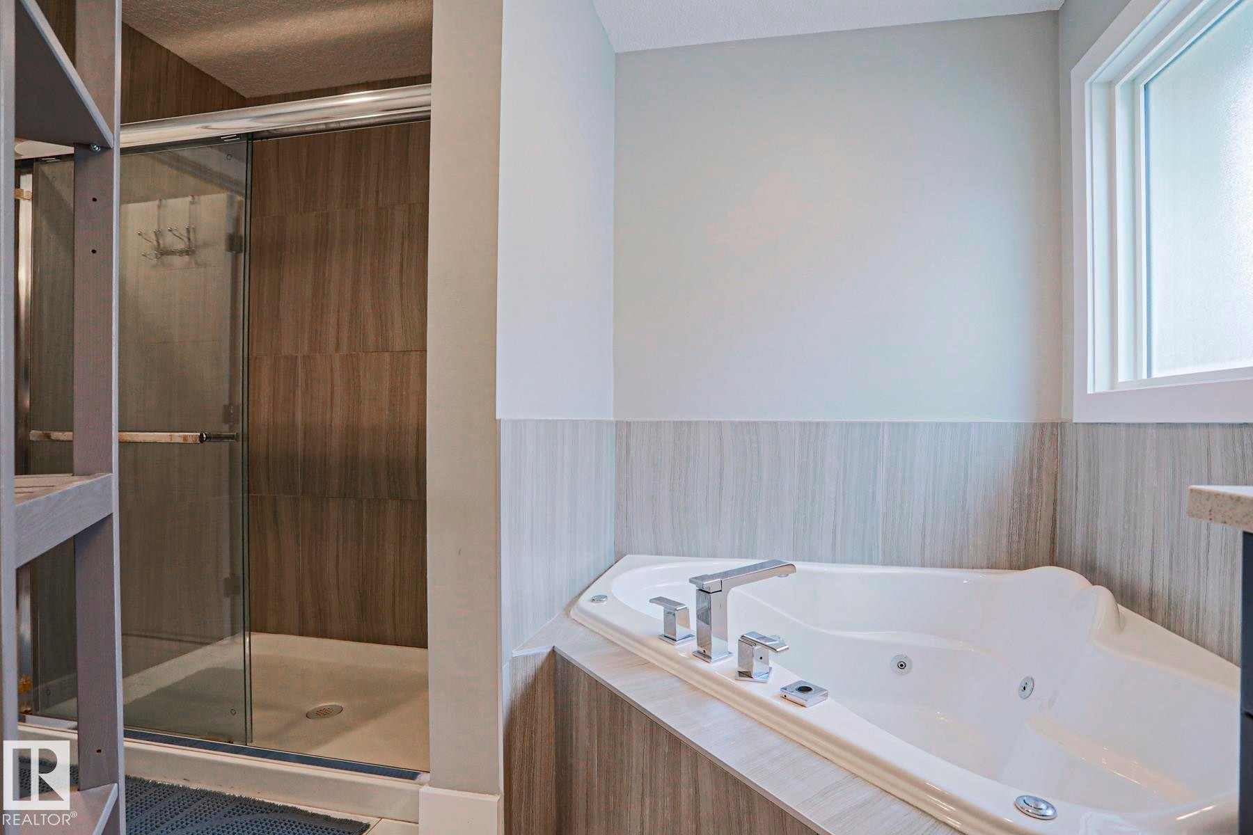 Soaking tub with a tiled surround, frosted window, and polished chrome fixtures - 1304 Ainslie Wynd Sw, Edmonton, AB - Indoor Photo Showing Bathroom