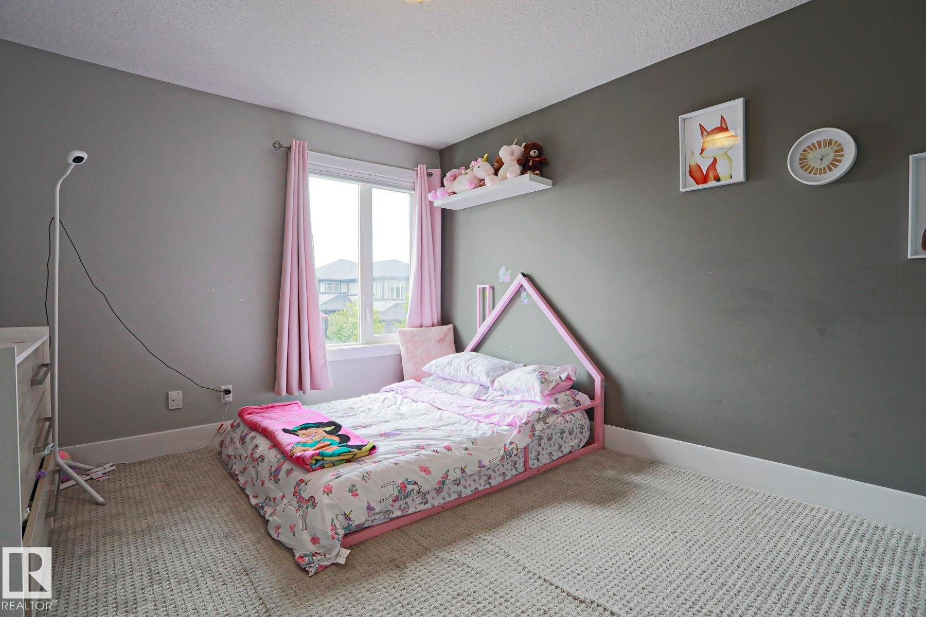Bedroom featuring a large window, neutral gray walls, textured carpeting, and white baseboards - 1304 Ainslie Wynd Sw, Edmonton, AB - Indoor Photo Showing Bedroom