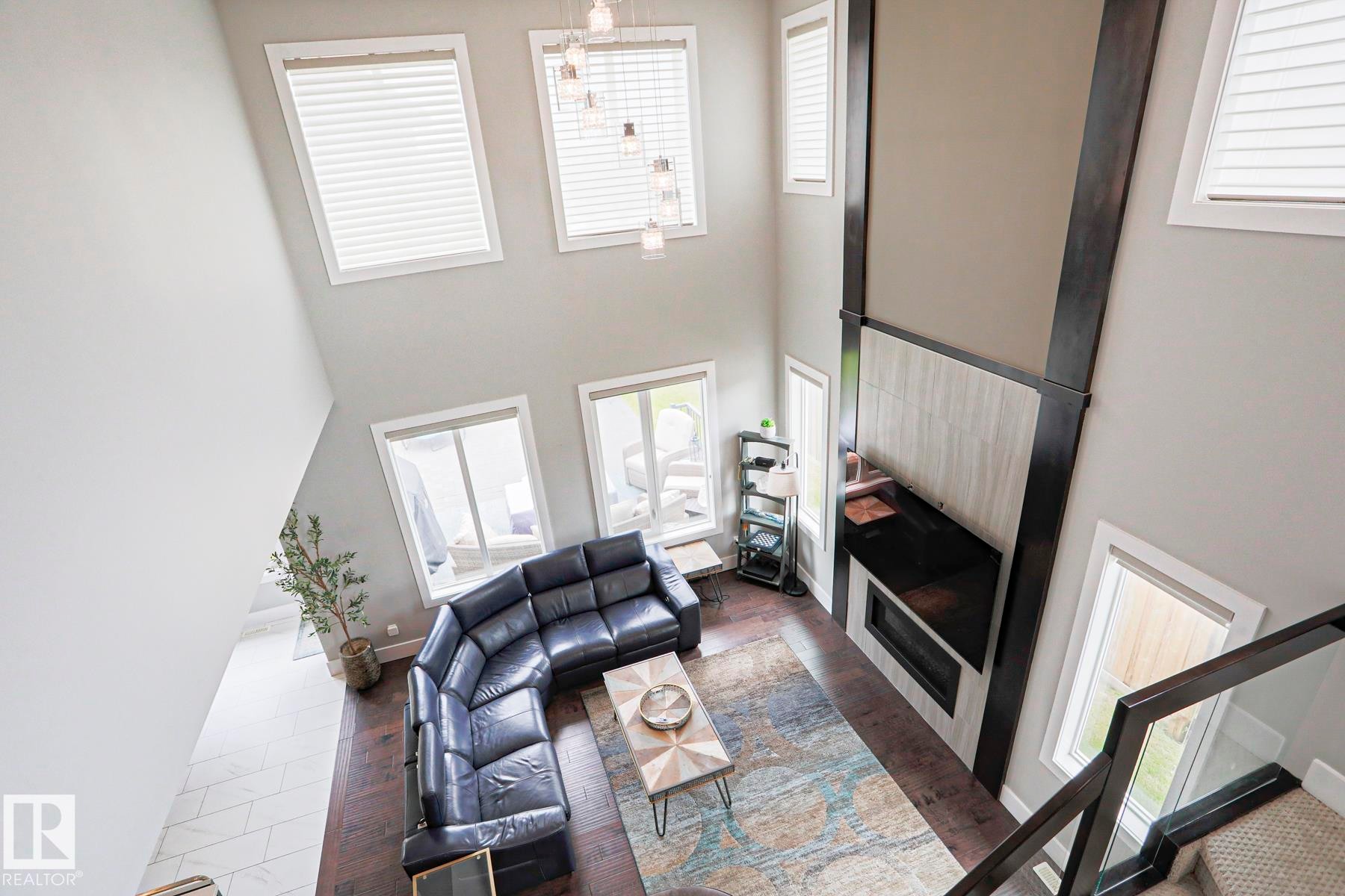 Double-height living area featuring a prominent fireplace with a dark mantel and light-toned tile surround - 1304 Ainslie Wynd Sw, Edmonton, AB - Indoor Photo Showing Other Room