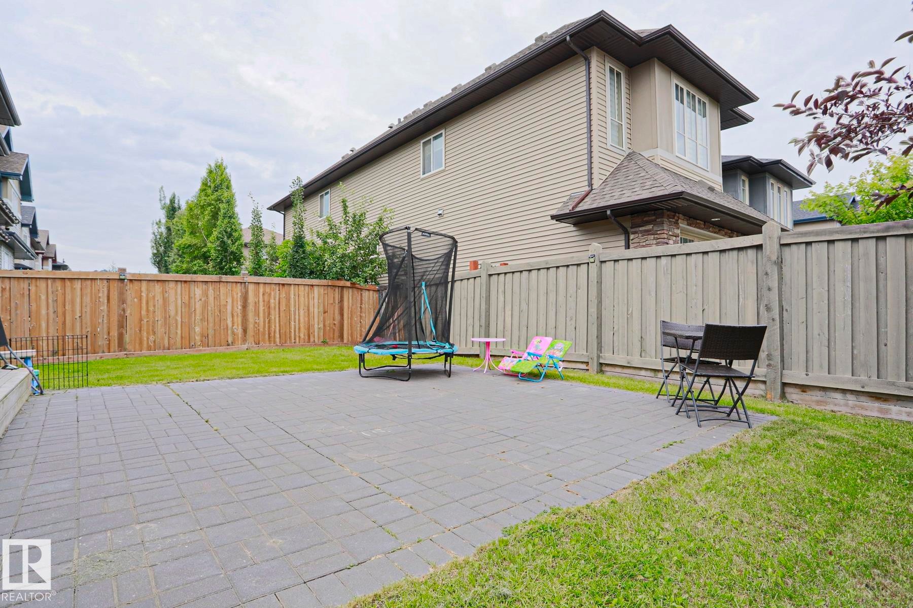 Expansive backyard featuring a large paver patio, a perimeter wood fence, and a manicured lawn area - 1304 Ainslie Wynd Sw, Edmonton, AB - Outdoor