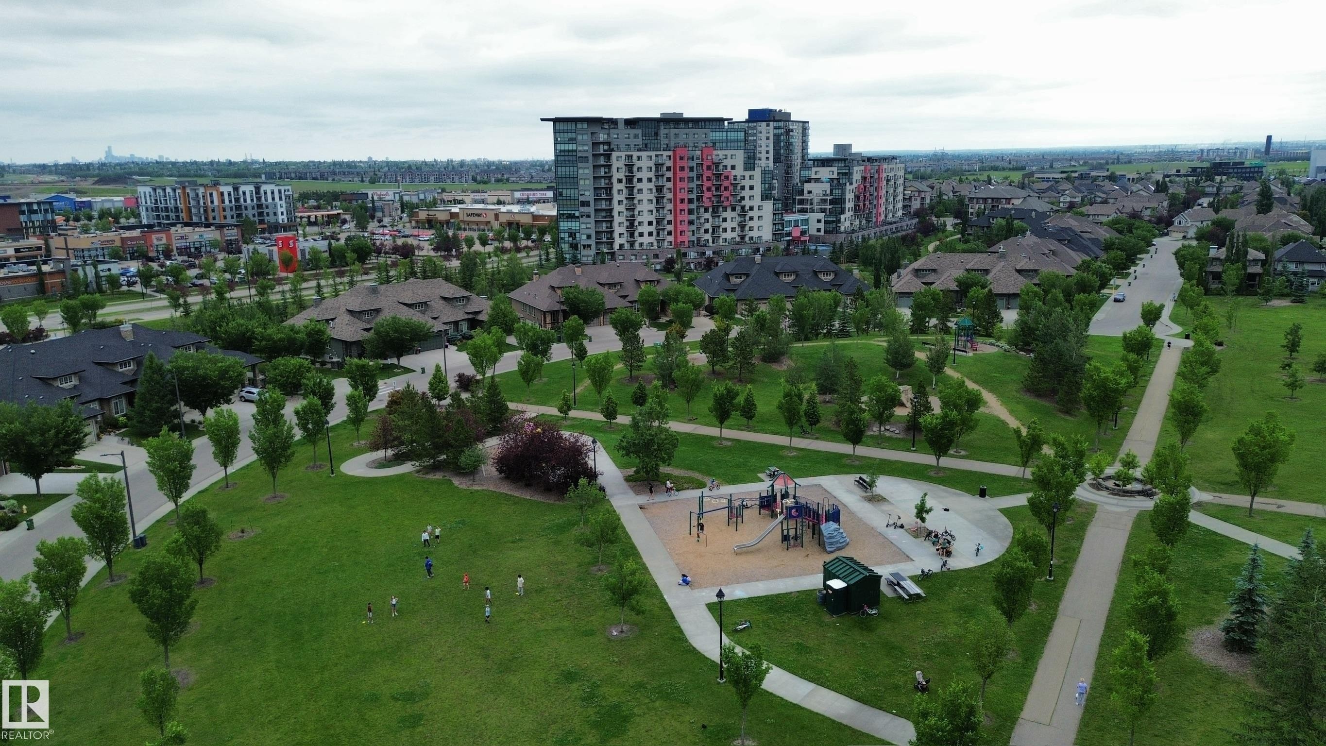 Expansive green space featuring a playground with multiple structures, concrete pathways, mature trees, and surrounding residential properties including multi-story buildings and single-family homes - 1304 Ainslie Wynd Sw, Edmonton, AB - Outdoor With View